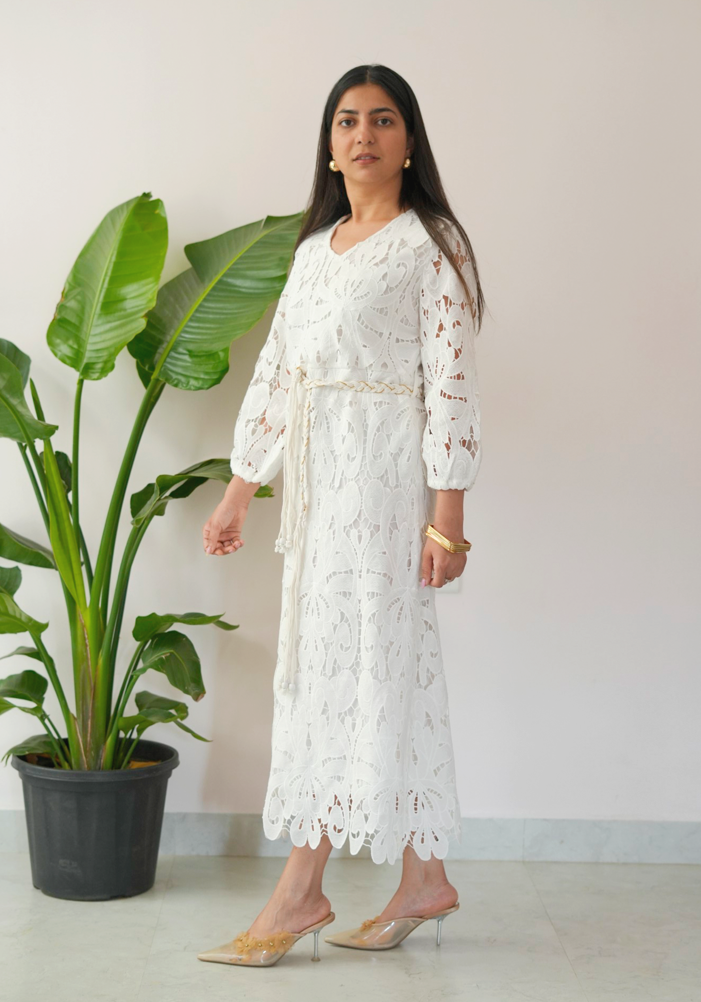 Woman in a white lace dress standing next to a potted plant.