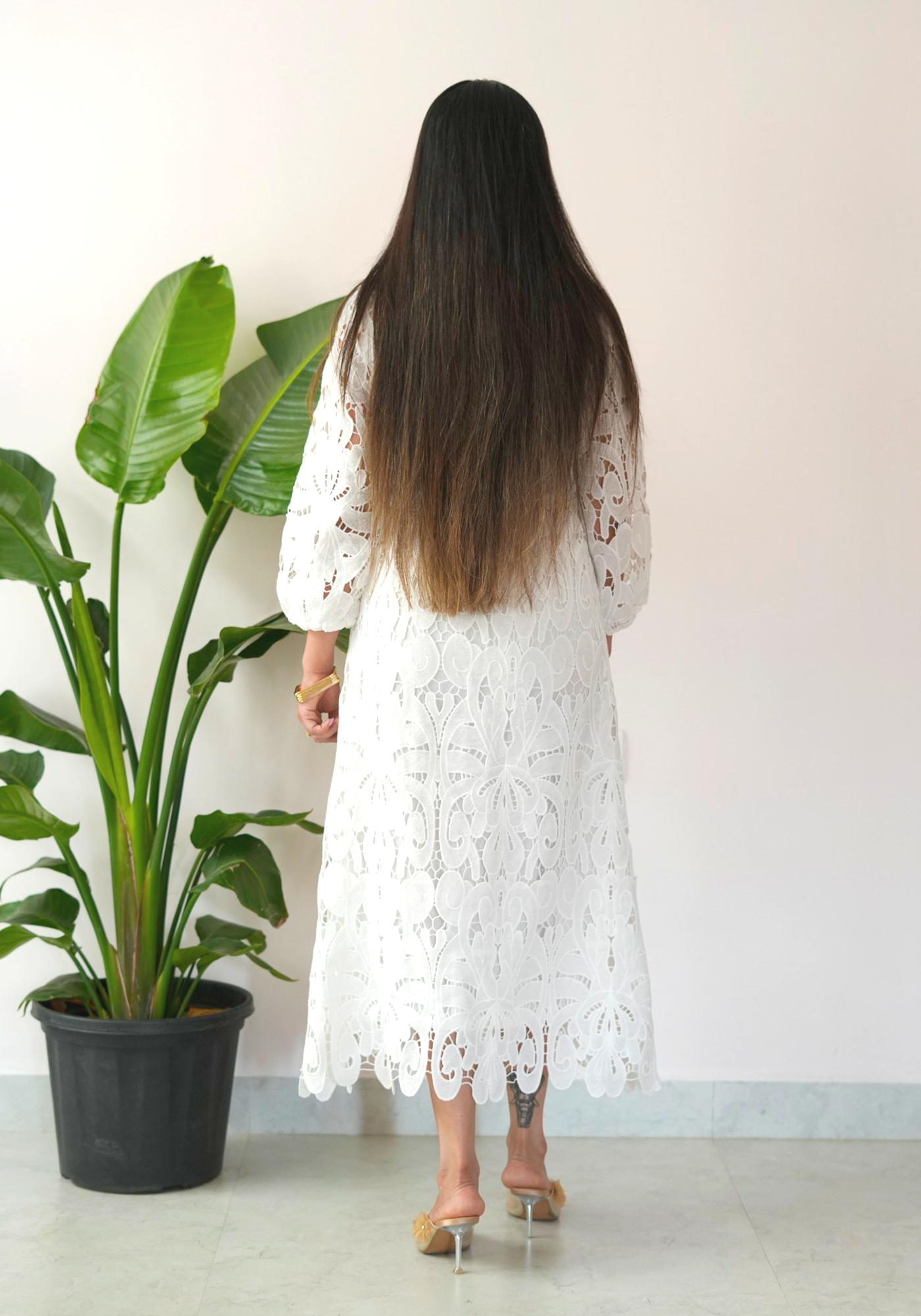 Woman in a white lace dress standing next to a potted plant.
