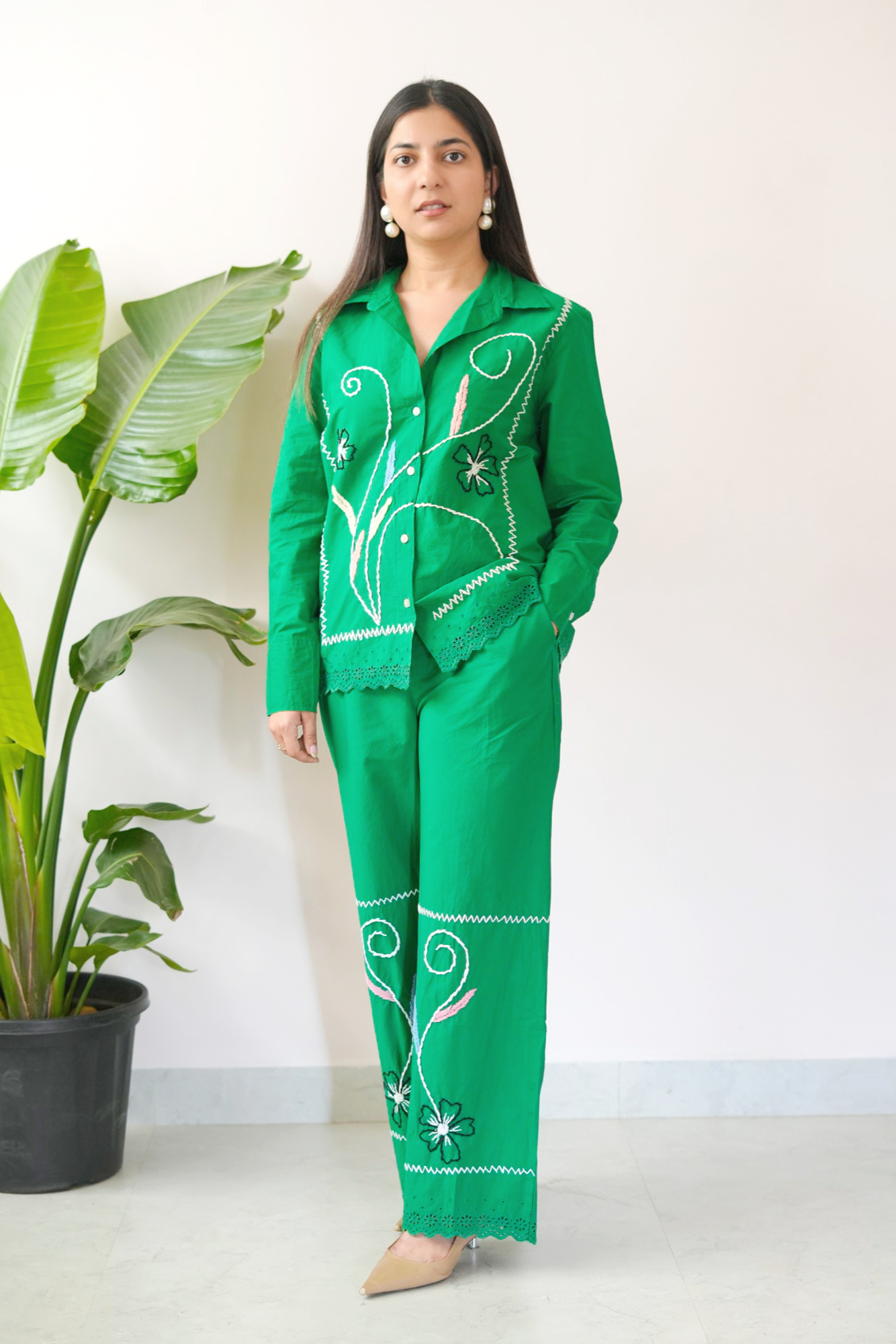 Woman wearing a green embroidered outfit standing next to a potted plant.