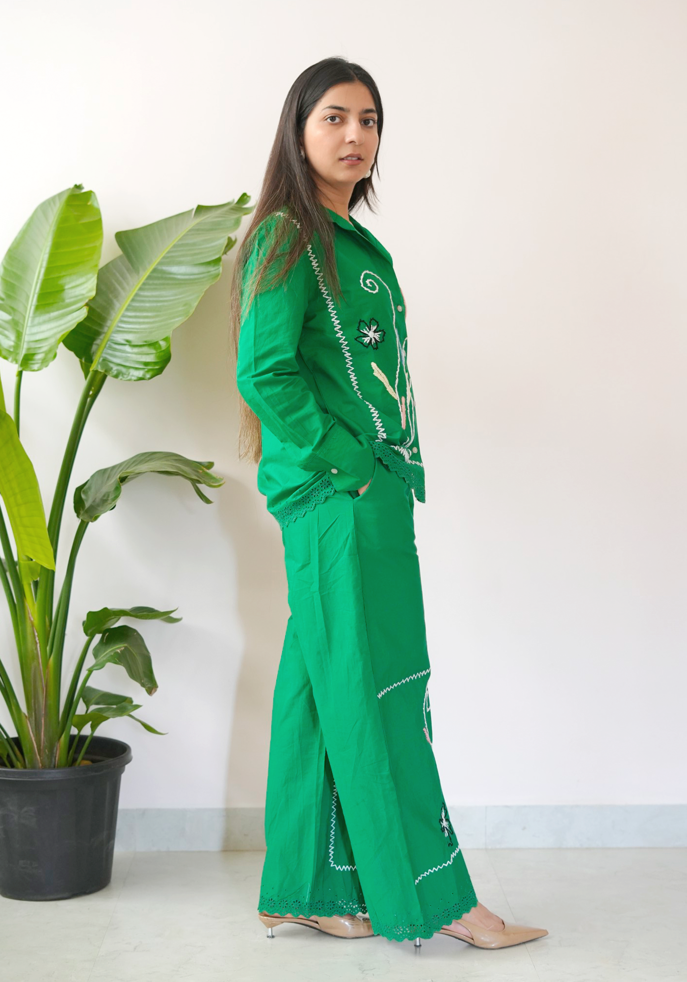 Woman in a green outfit standing next to a potted plant against a white background.