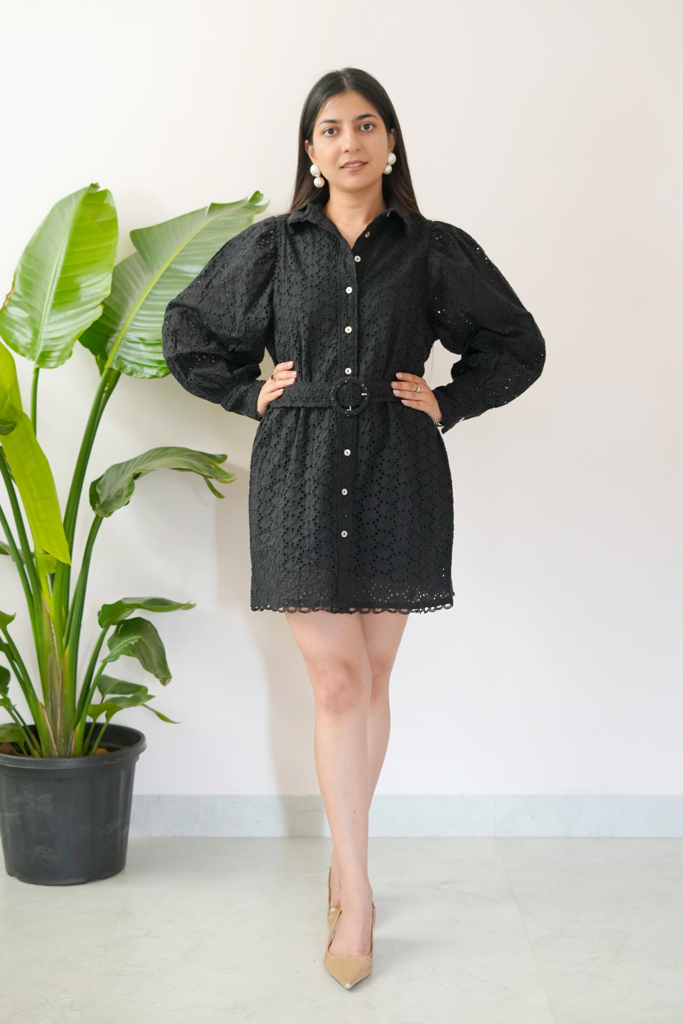 Woman wearing a black dress standing next to a potted plant against a white wall