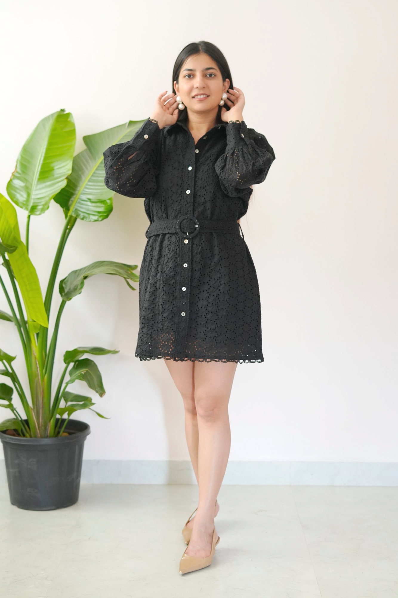Woman wearing a black dress standing next to a potted plant indoors.