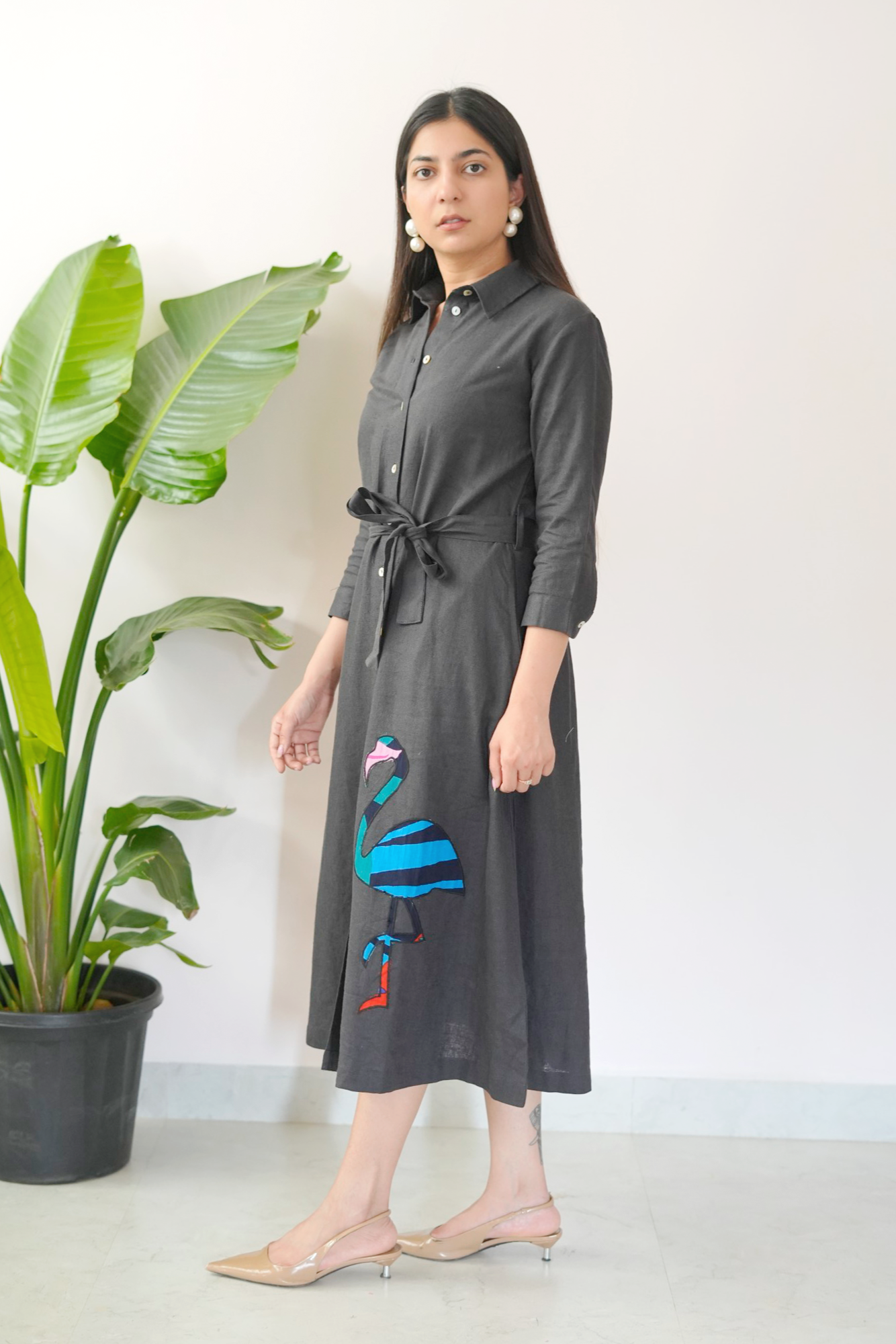 Woman wearing a dark gray dress with colorful bird design in a minimal indoor setting.