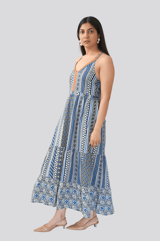Woman wearing a blue and white patterned dress standing against a white wall with green leaves.