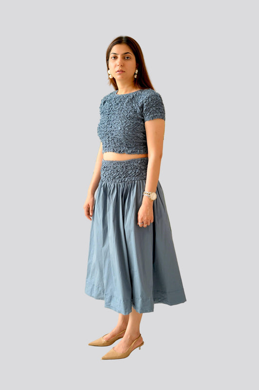 Woman wearing a blue top and skirt set on a light gray background