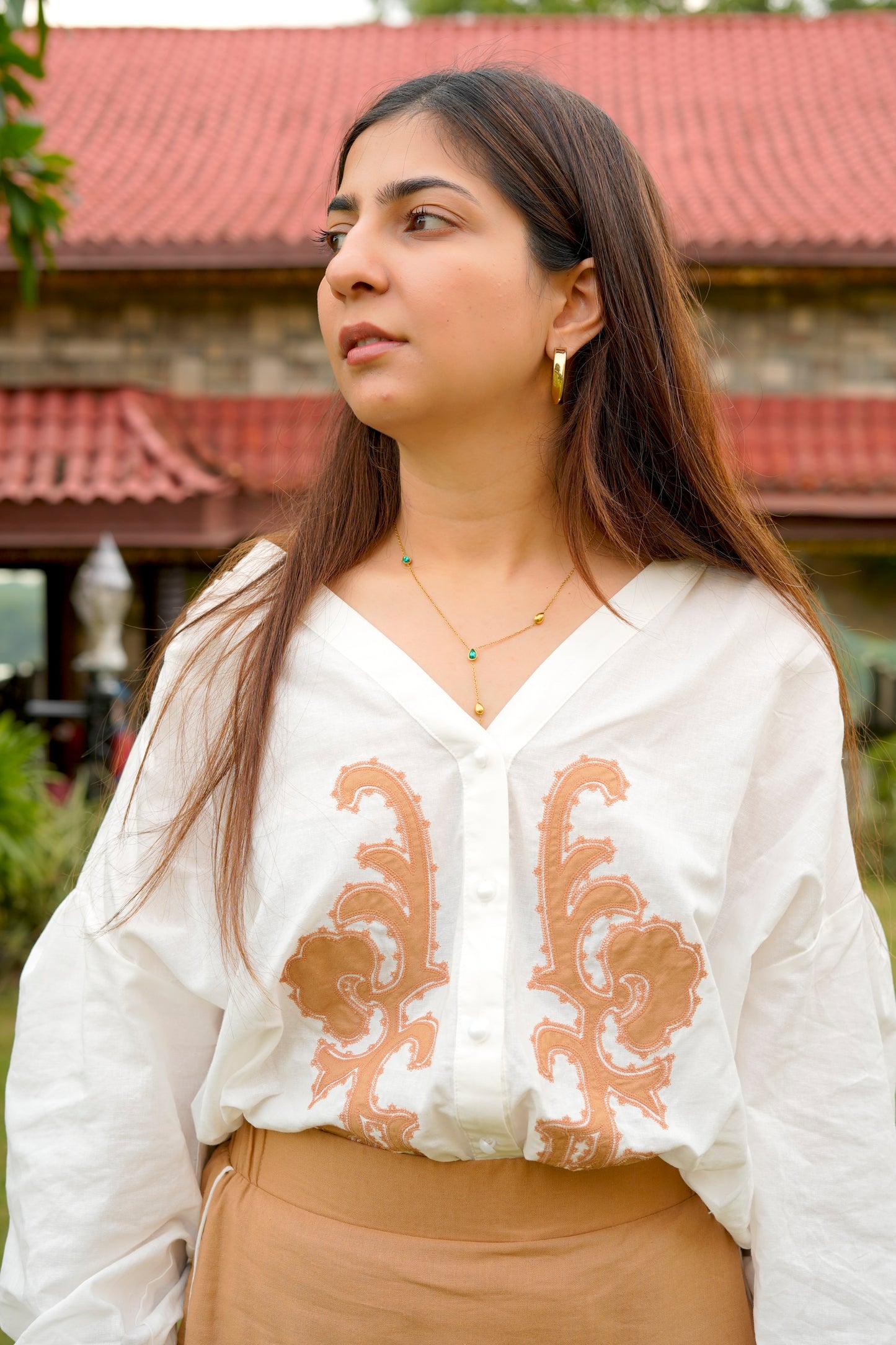 Woman wearing a white blouse with brown embroidery and beige pants outdoors.