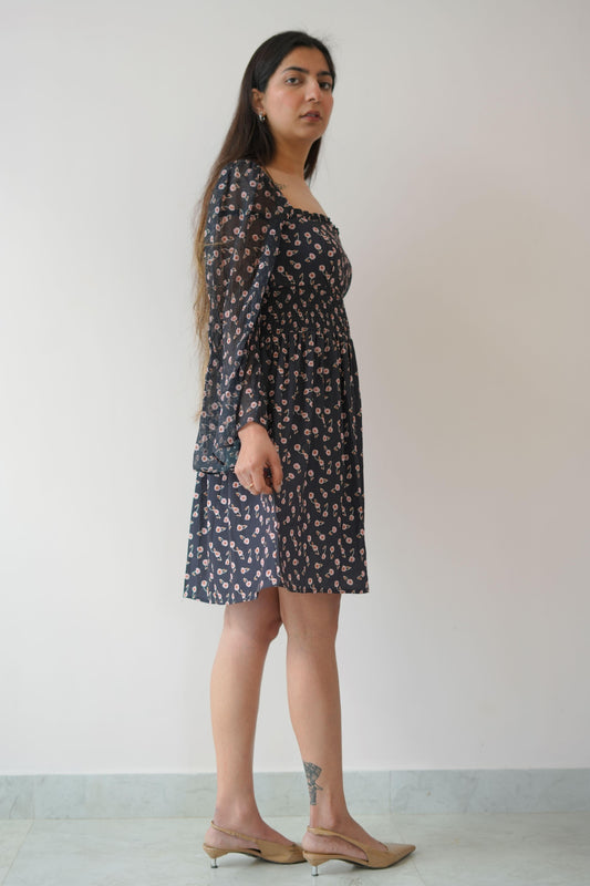 Woman wearing a black floral dress standing against a white wall