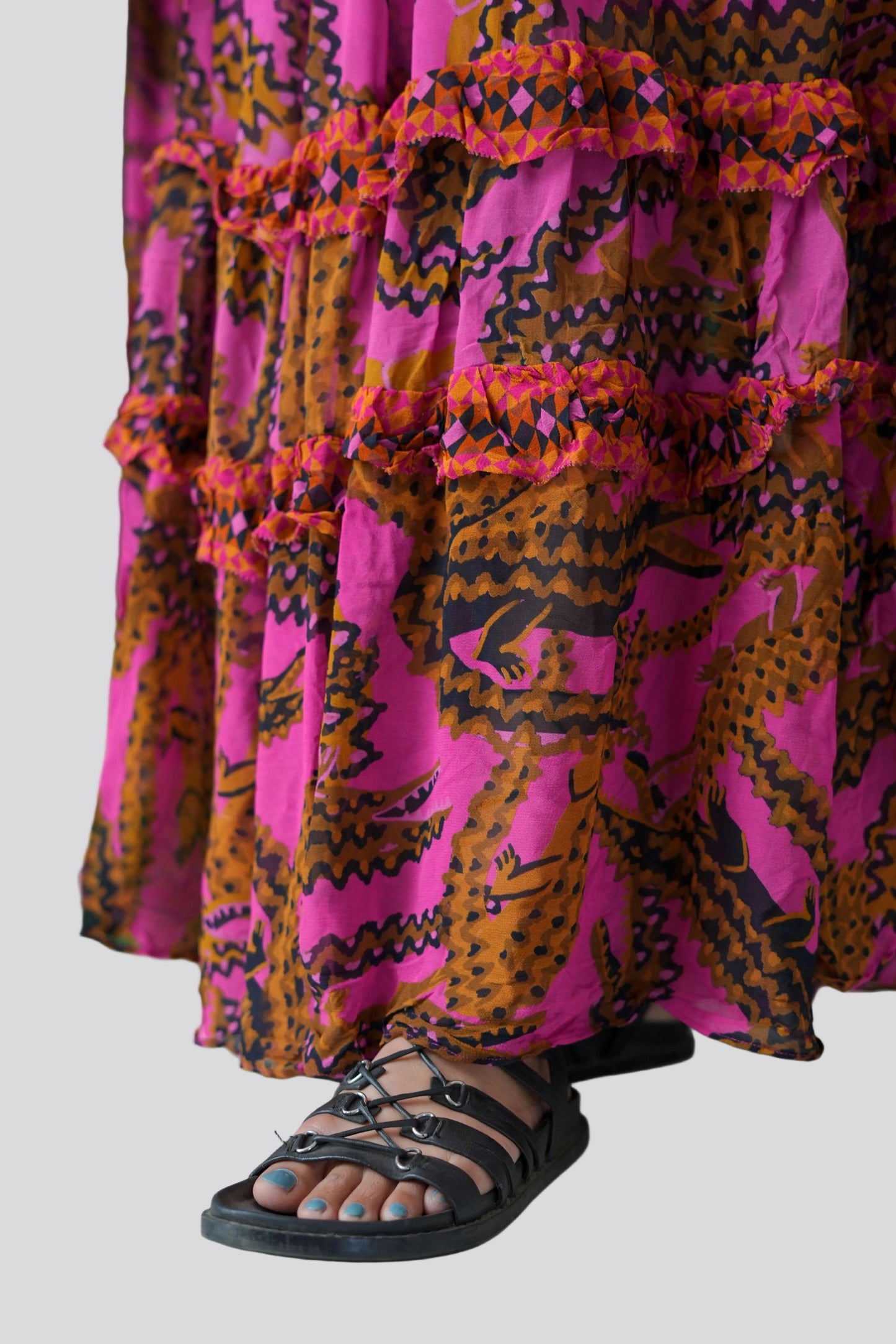 Person wearing a vibrant pink and orange patterned dress with black sandals on a light gray background