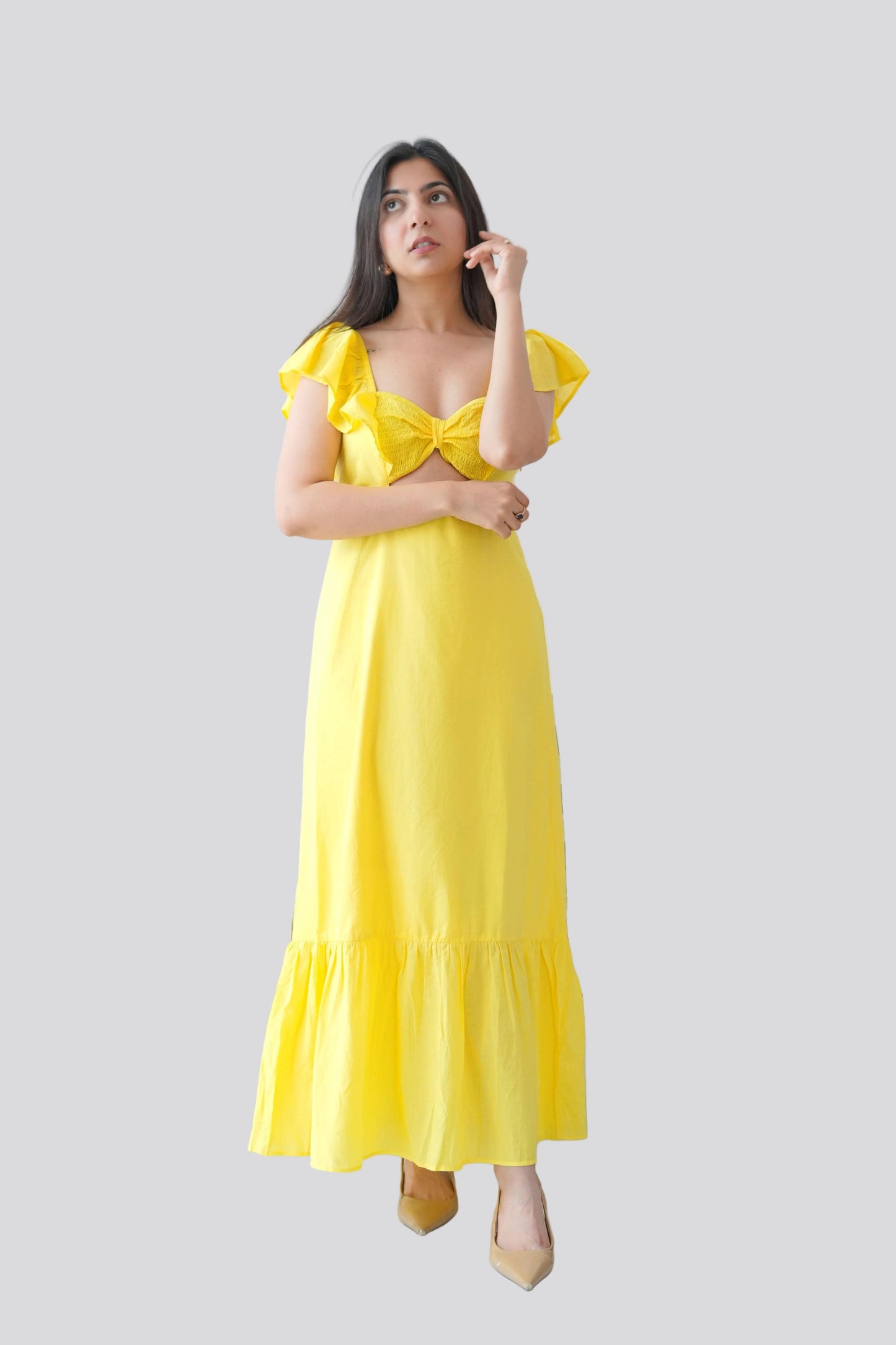 Woman wearing a yellow dress with ruffled sleeves on a light gray background