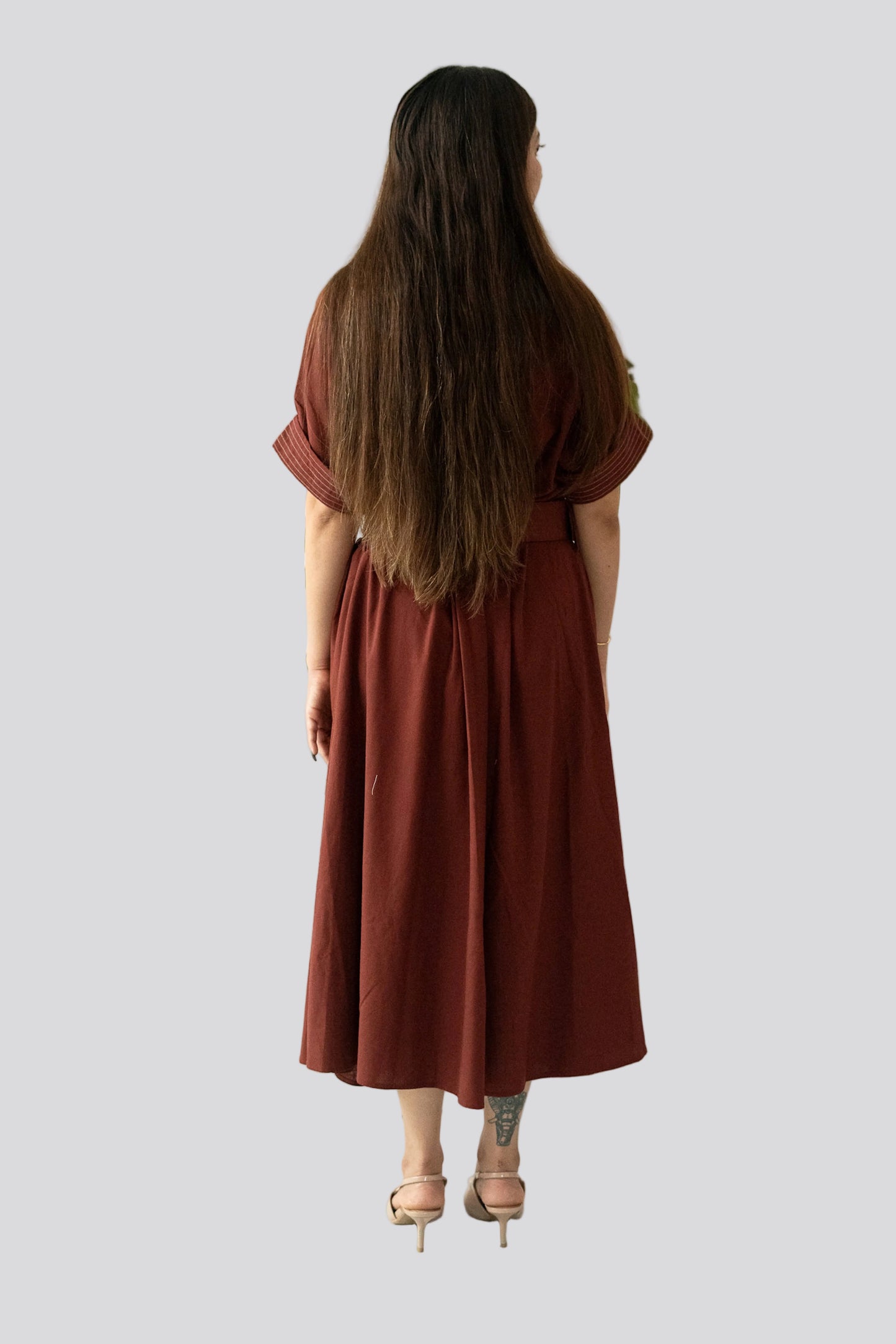Woman wearing a rust-colored dress standing in front of a white wall with green plants.