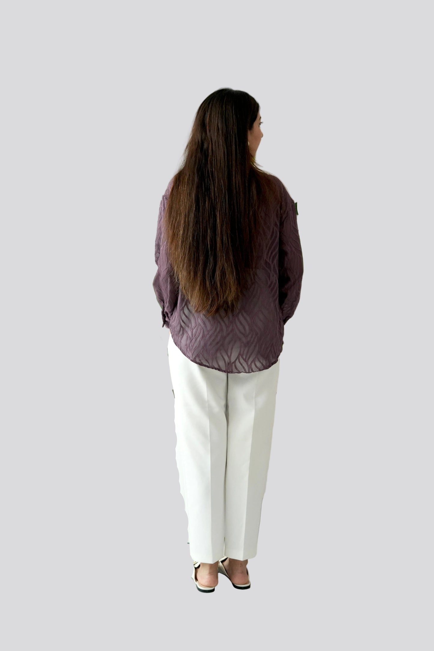 Person wearing a purple shirt and white pants standing against a plain background