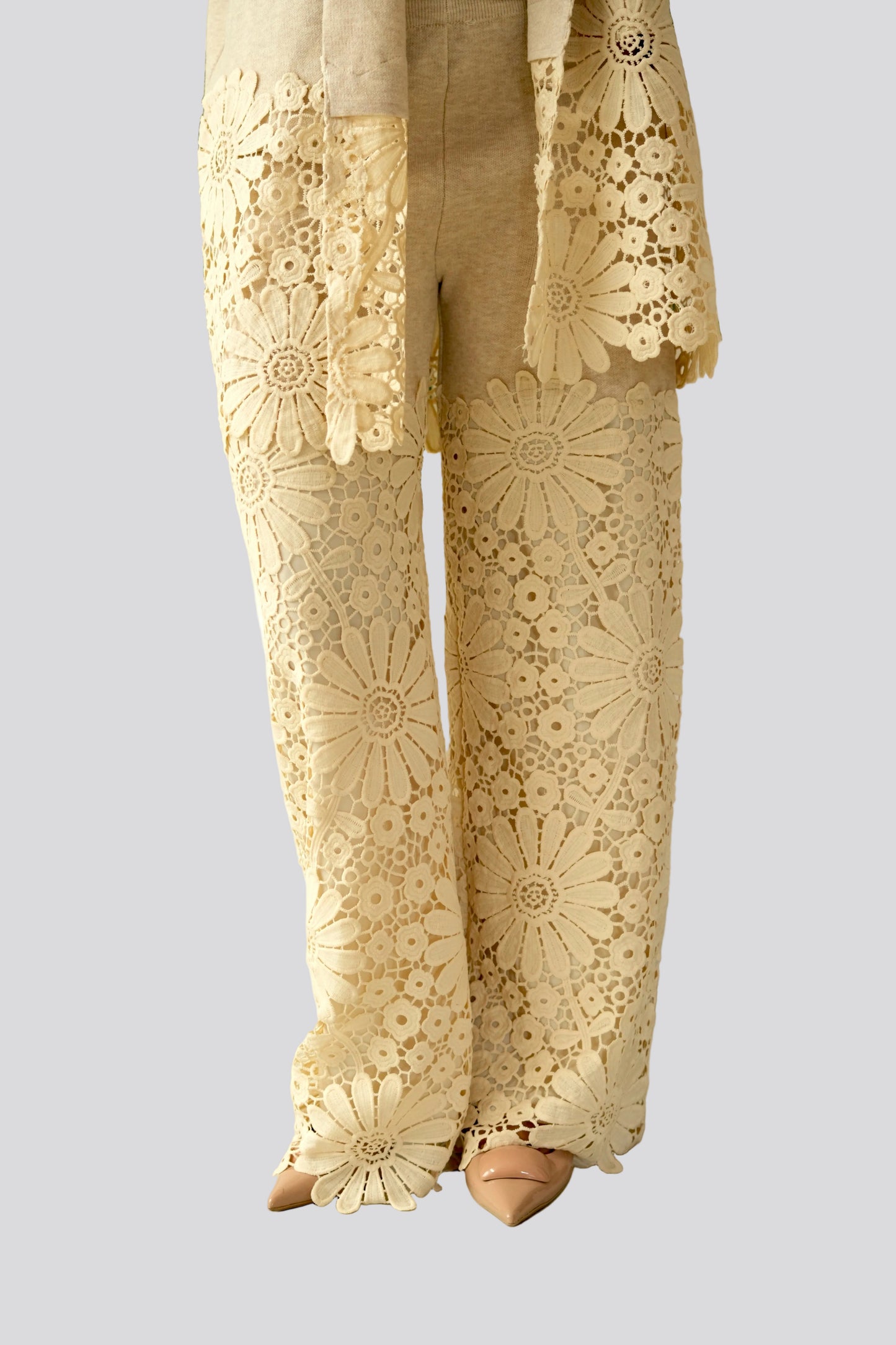 Beige lace pants with floral patterns worn by a person, standing against a plain background.
