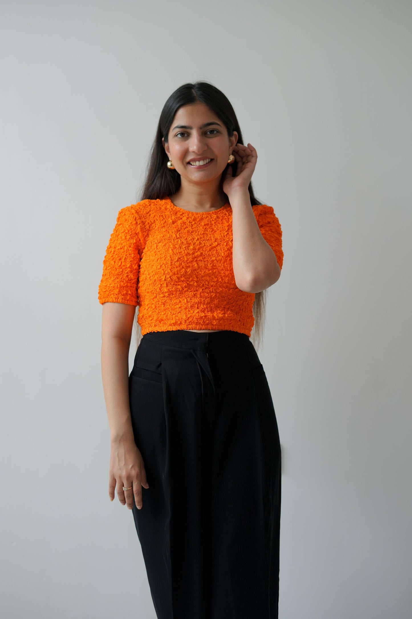 Woman wearing an orange top and black pants on a plain background