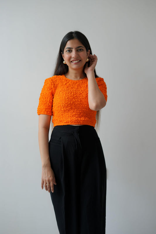 Woman wearing an orange top and black pants on a plain background