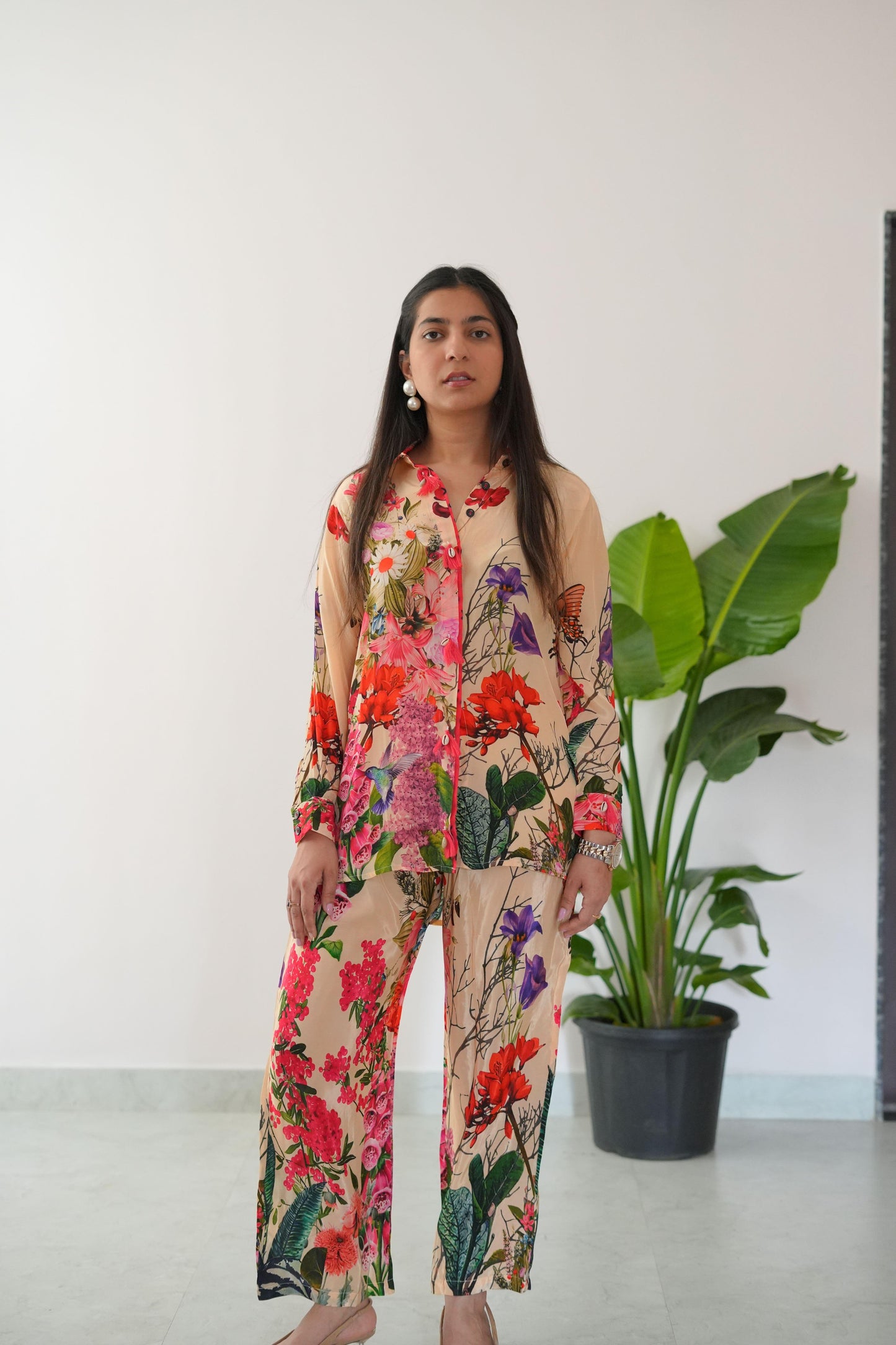 Woman wearing a floral dress standing in front of a white wall with a plant.
