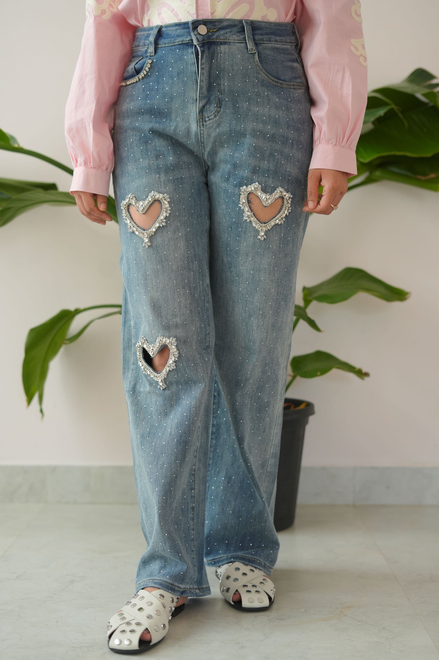 Person wearing ripped blue jeans and a pink jacket with a white background