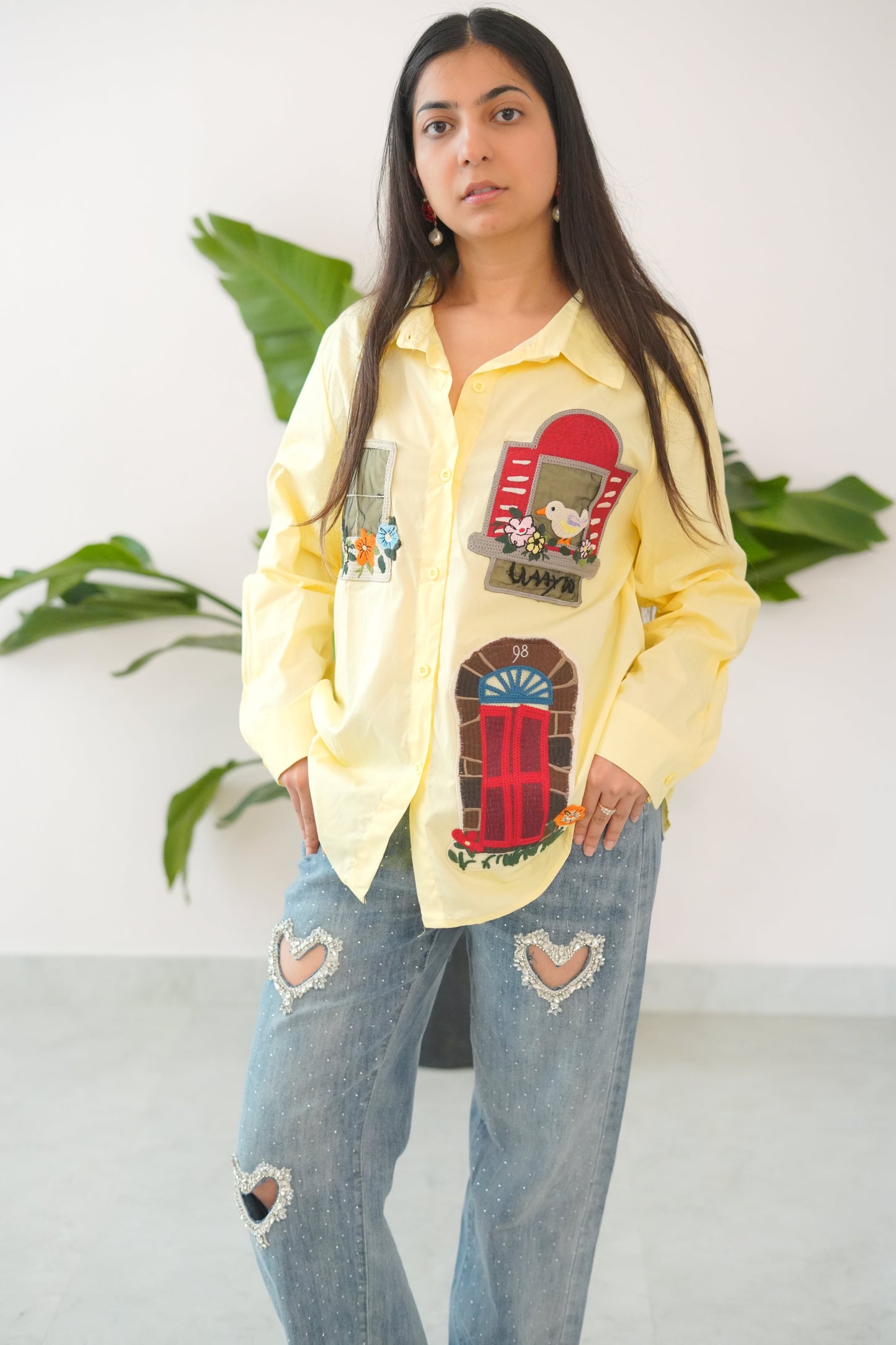 Person wearing a yellow sweatshirt with colorful designs and ripped jeans, standing against a white background.