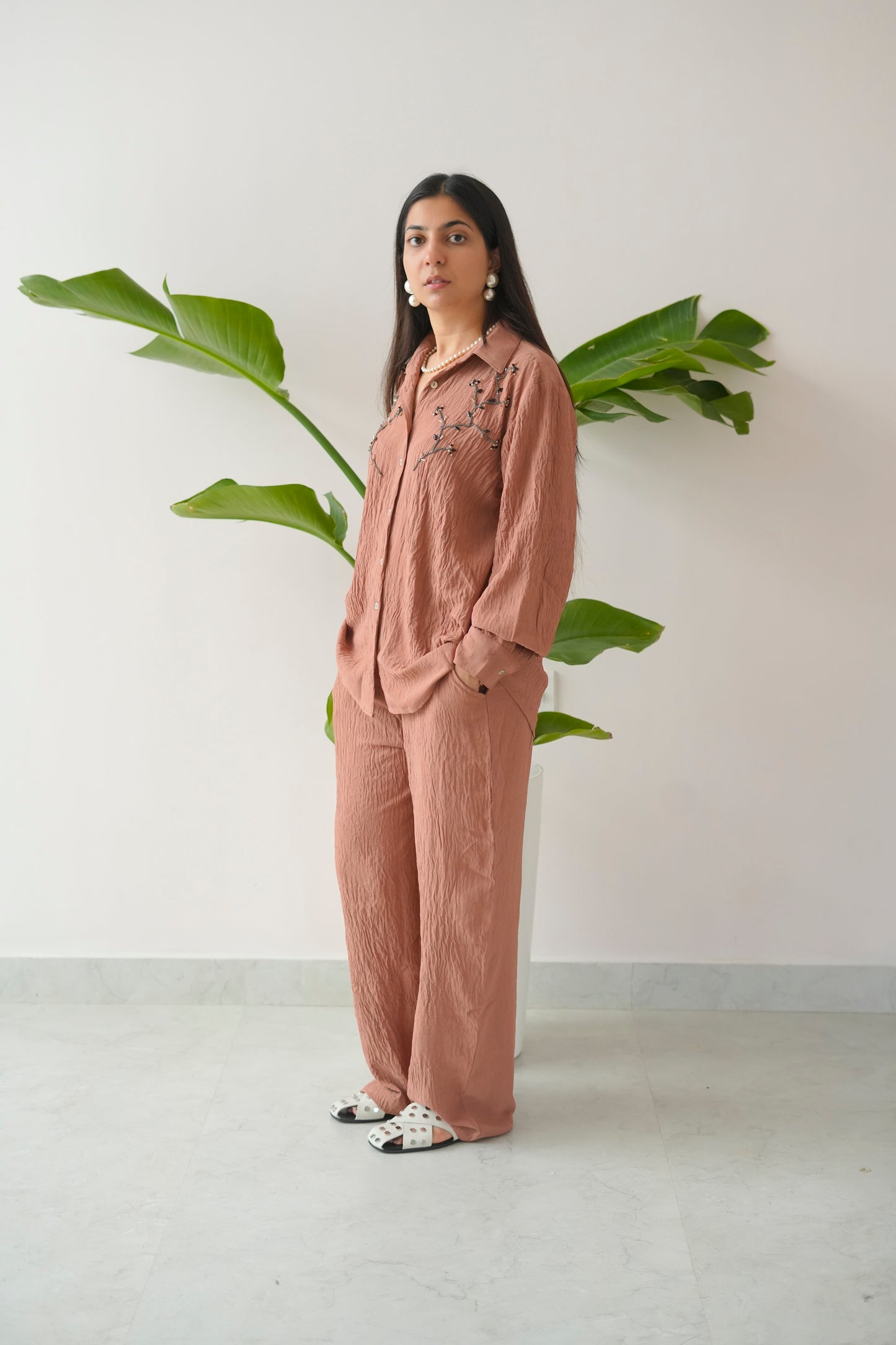 Woman in a pink outfit standing next to a plant against a white wall