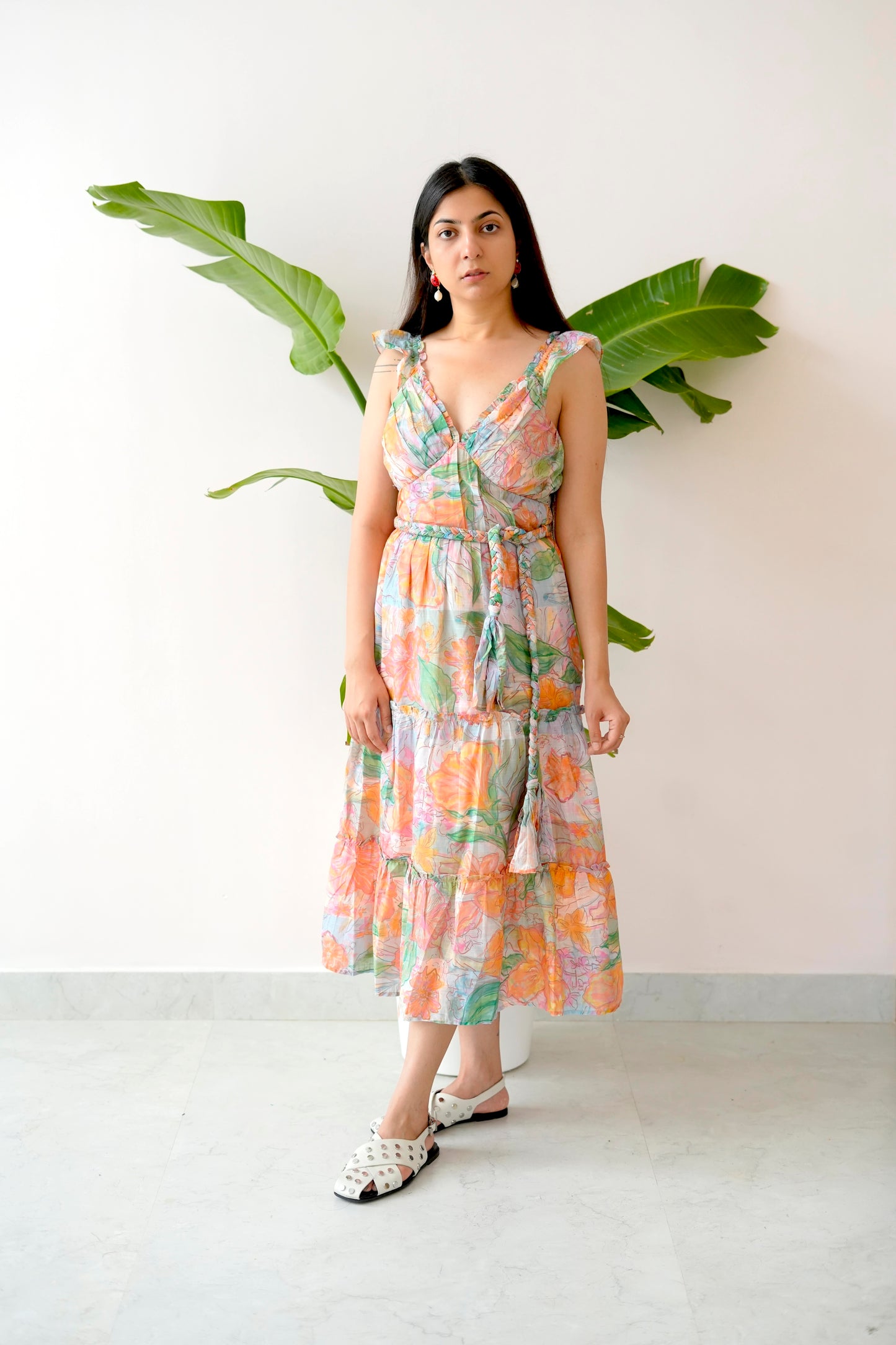 Woman wearing a floral dress standing against a white wall with green leaves.