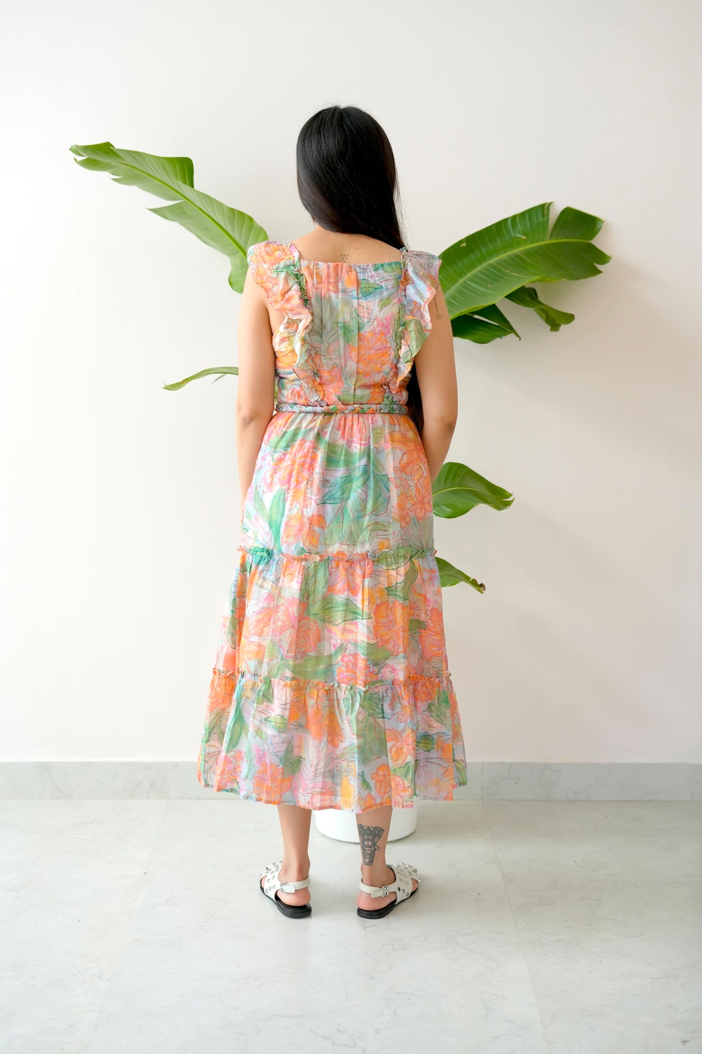 Woman wearing a colorful dress standing in front of a white wall with a plant.