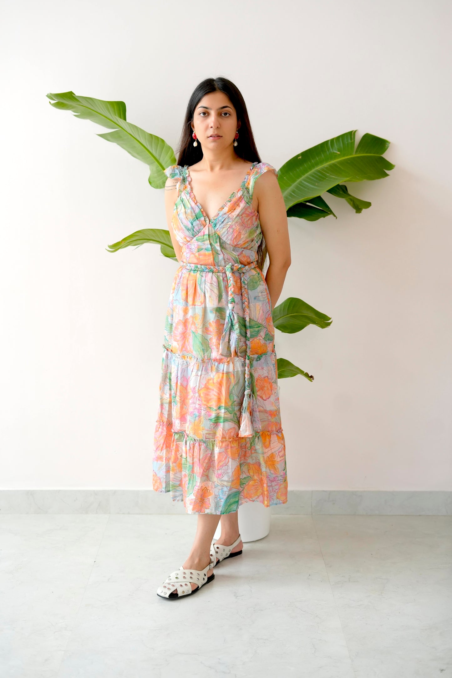 Woman wearing a floral dress standing against a white wall with a plant.