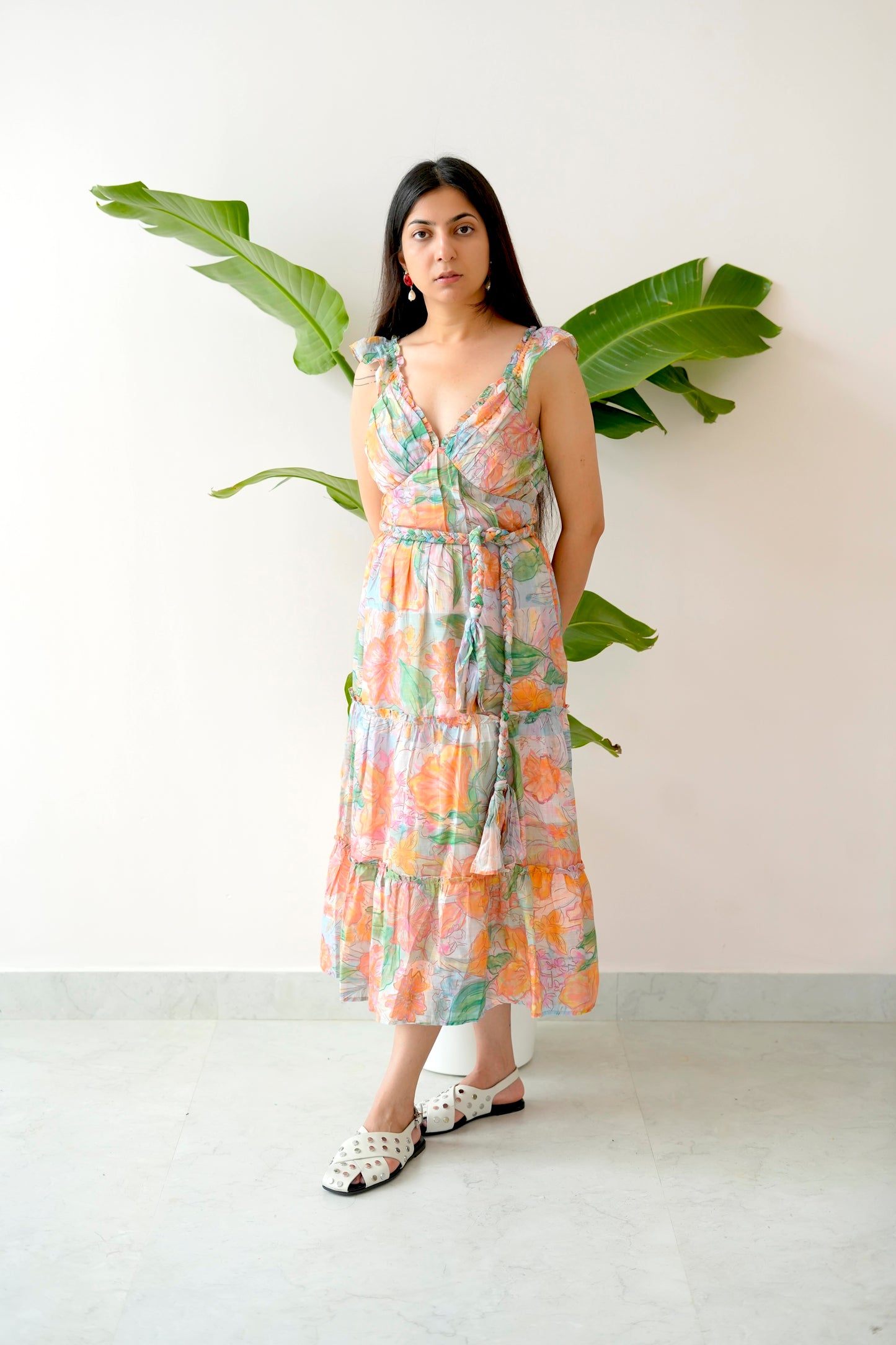 Woman wearing a floral dress standing against a white wall with green leaves.