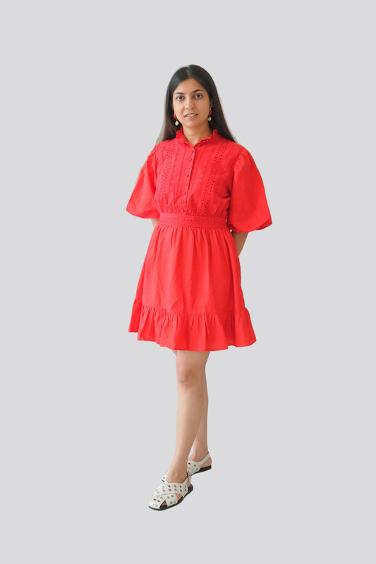 Woman wearing a red dress standing in front of a white wall with green leaves.