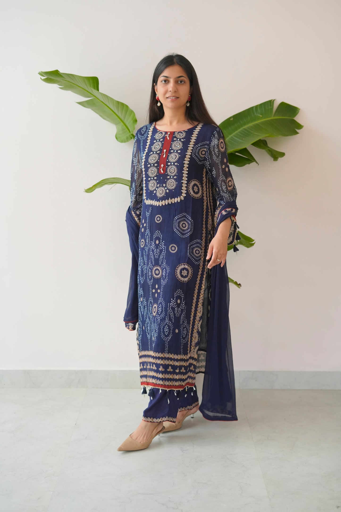 Woman wearing a blue embroidered traditional outfit with a white background and green leaves.
