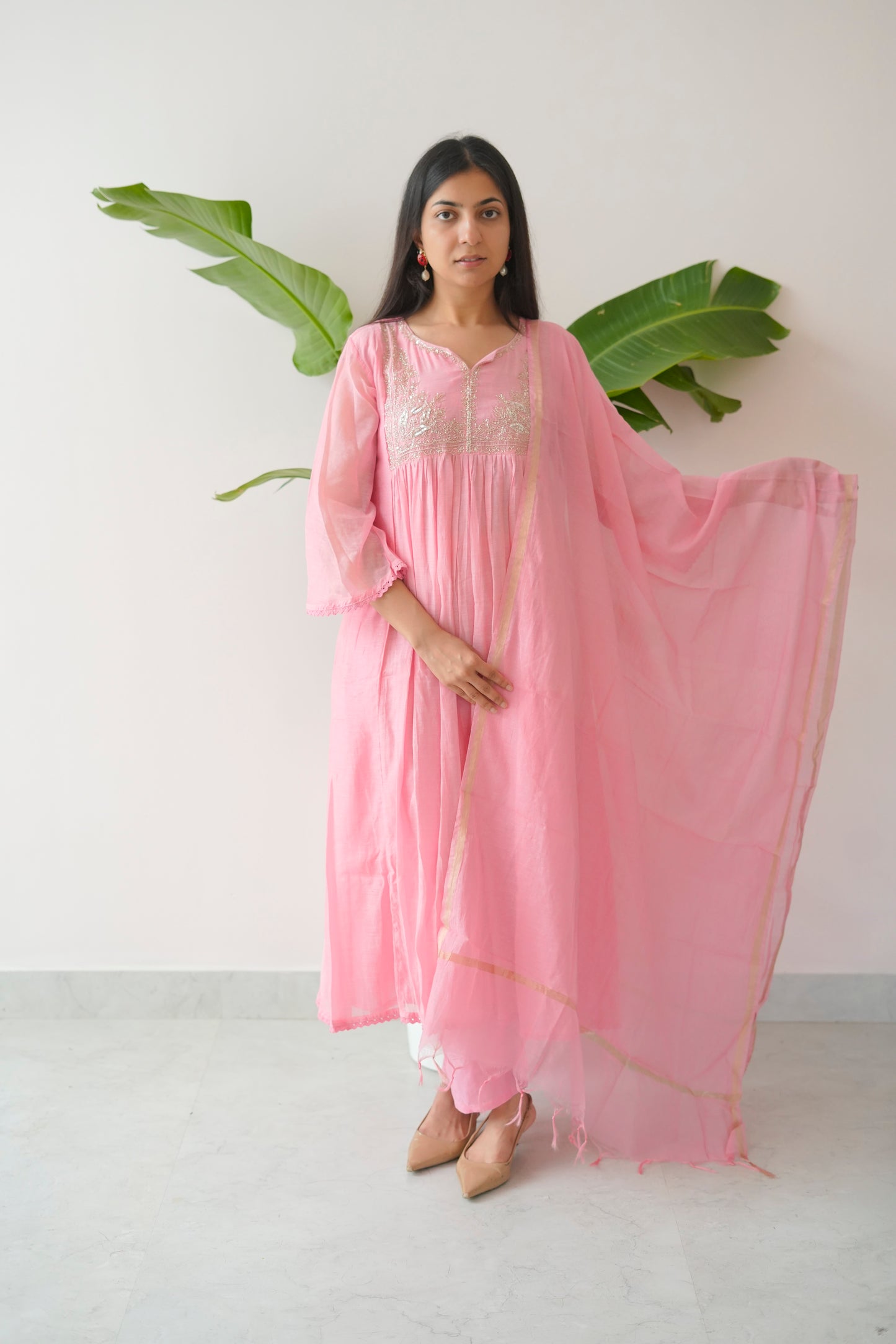 Woman wearing a pink traditional outfit with a white background and green leaves.