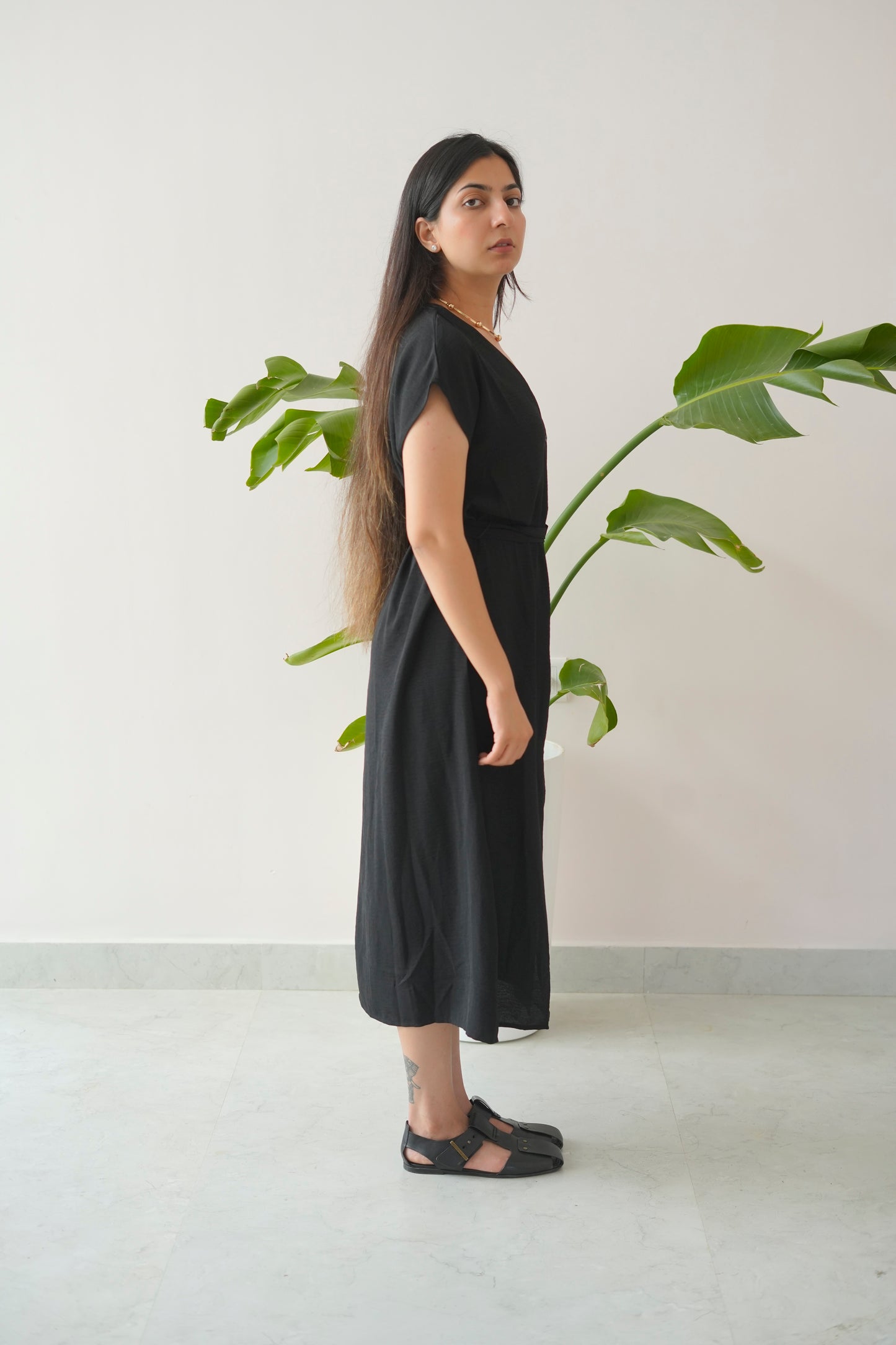 Woman wearing a black dress standing next to a plant indoors.