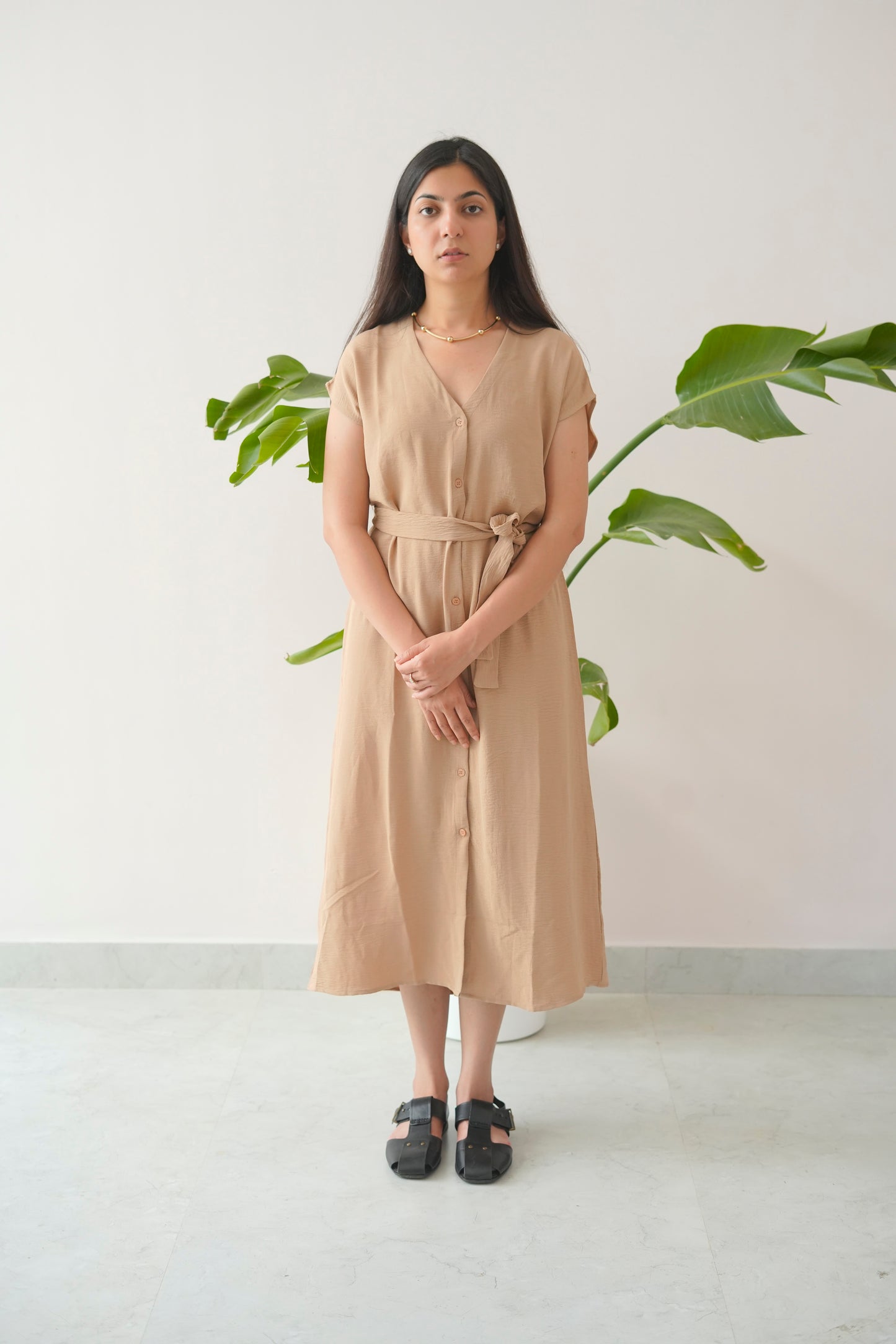 Woman wearing a beige dress standing in front of a plant with a white background