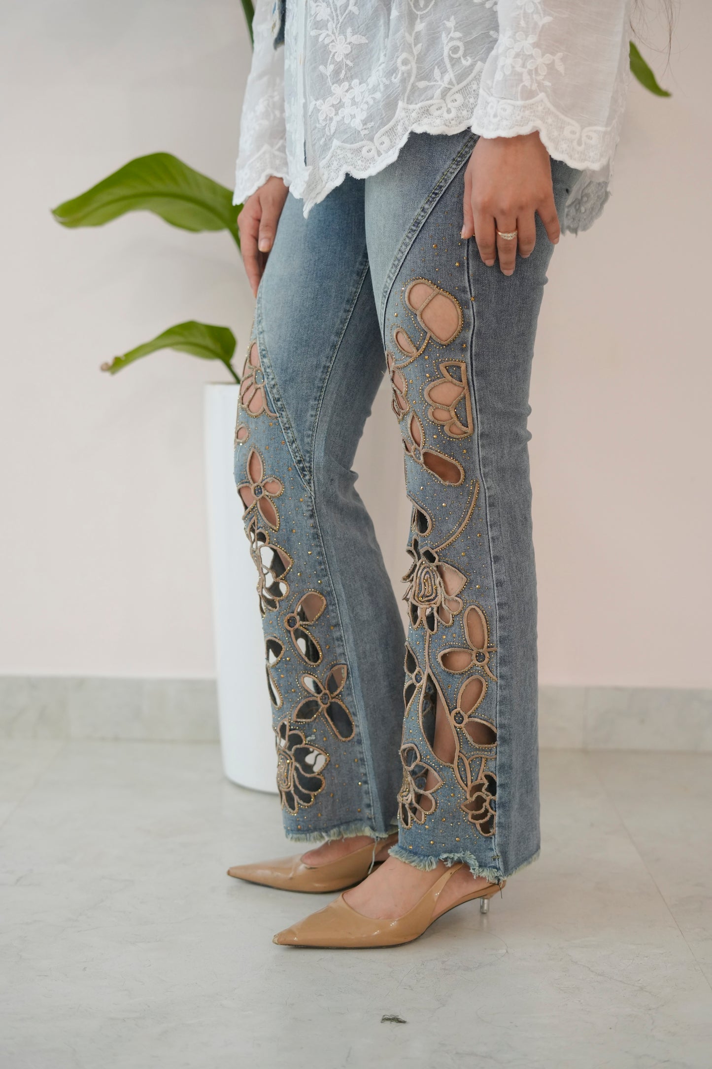 Person wearing floral embroidered jeans with a white lace top against a neutral background