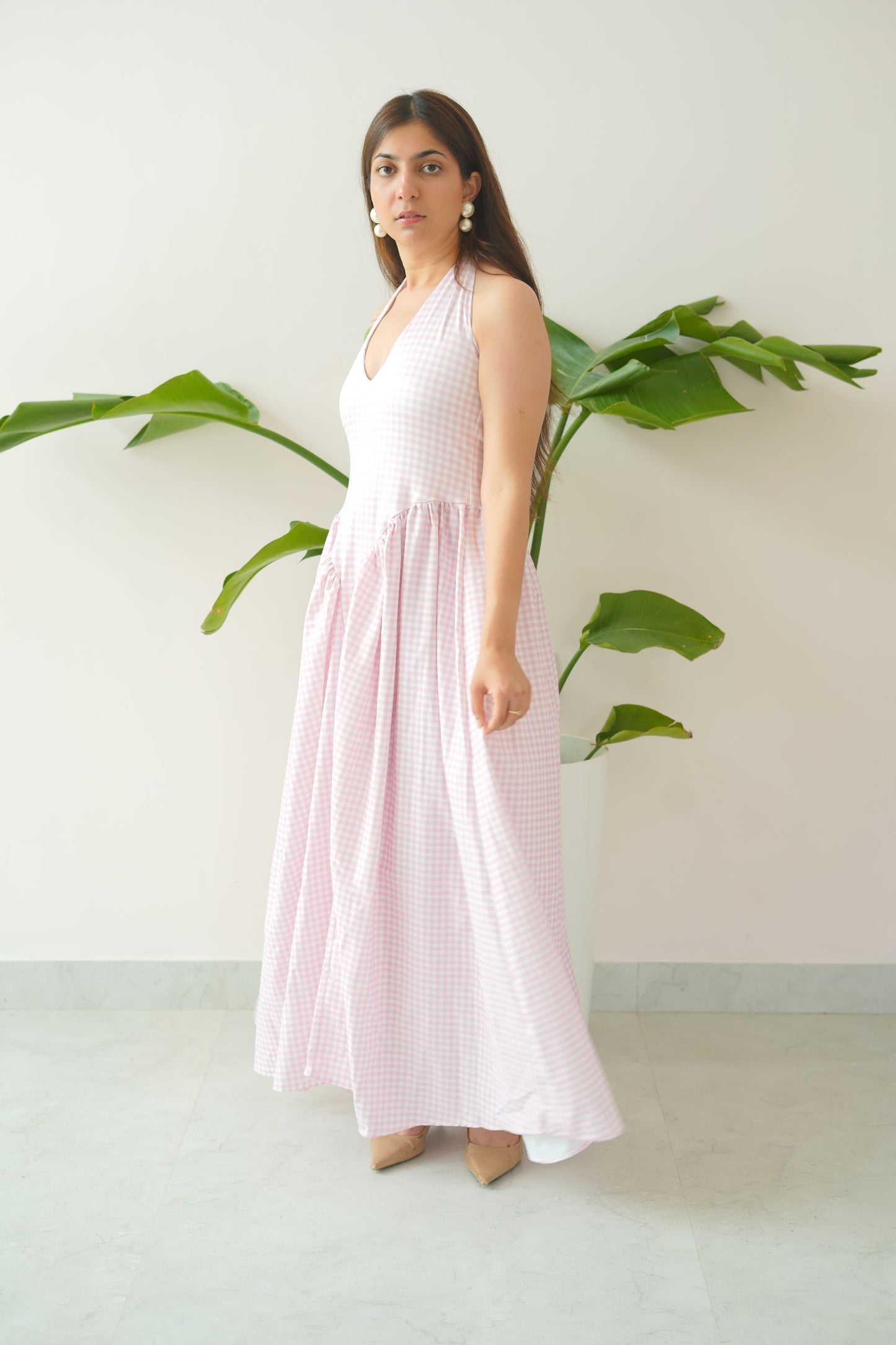 Woman in a pink dress standing next to green leaves on a white background