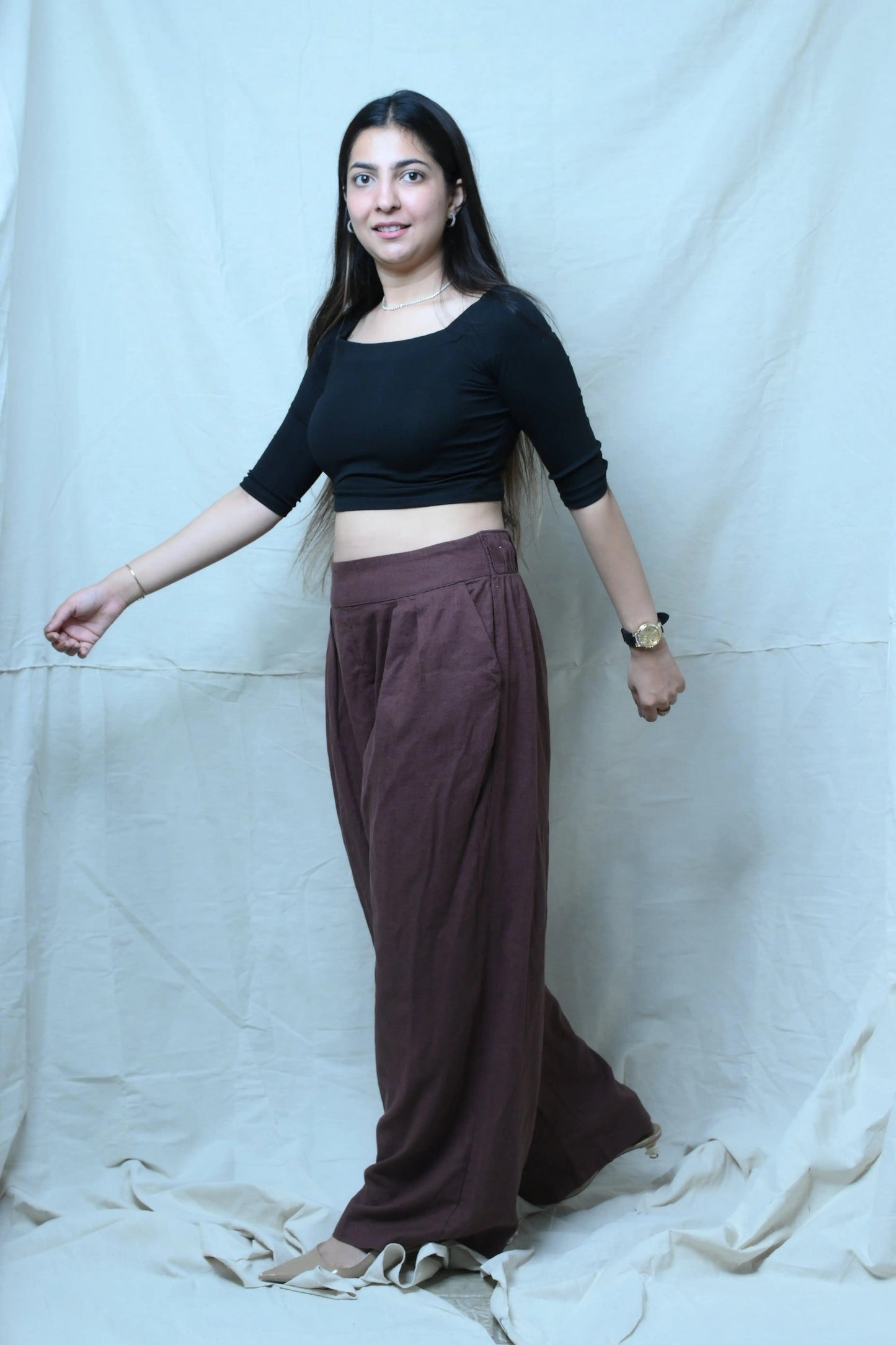 Woman wearing a black top and brown pants against a white background