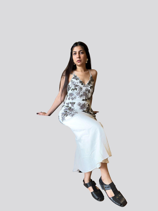 Woman wearing a floral top and white skirt with black shoes on a plain background