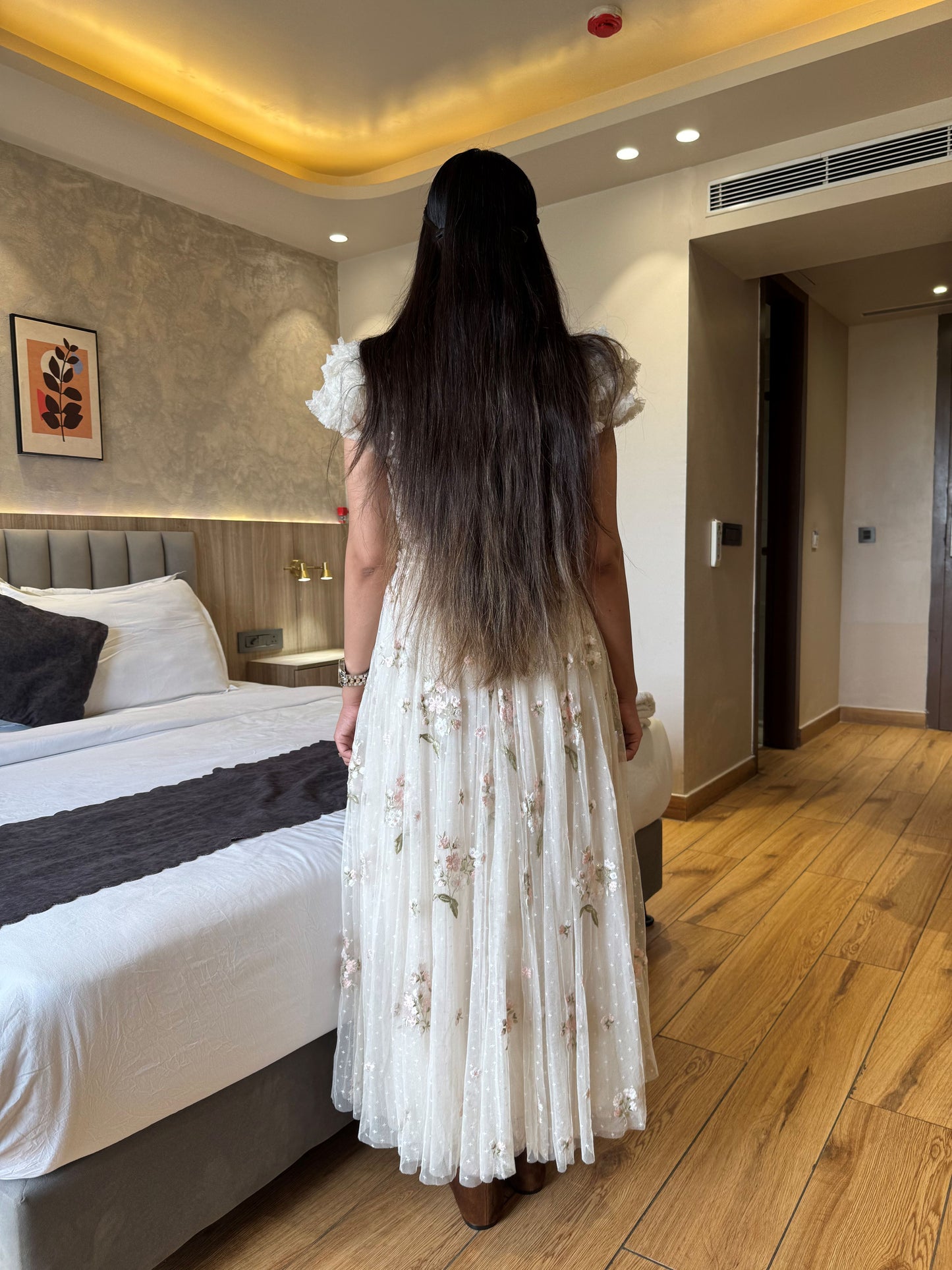 Woman in a white dress standing in a bedroom looking at a bed.