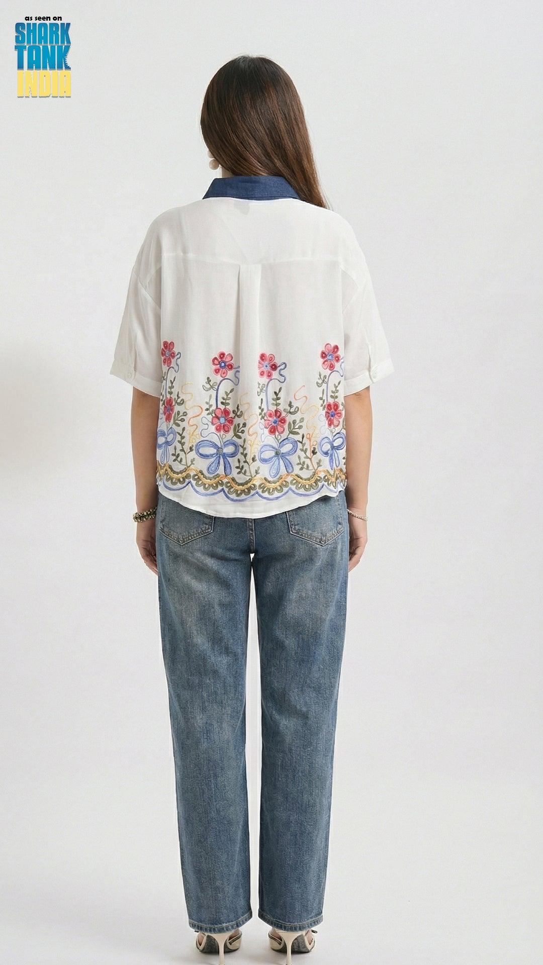 Woman wearing a white blouse with floral embroidery and blue jeans on a white background