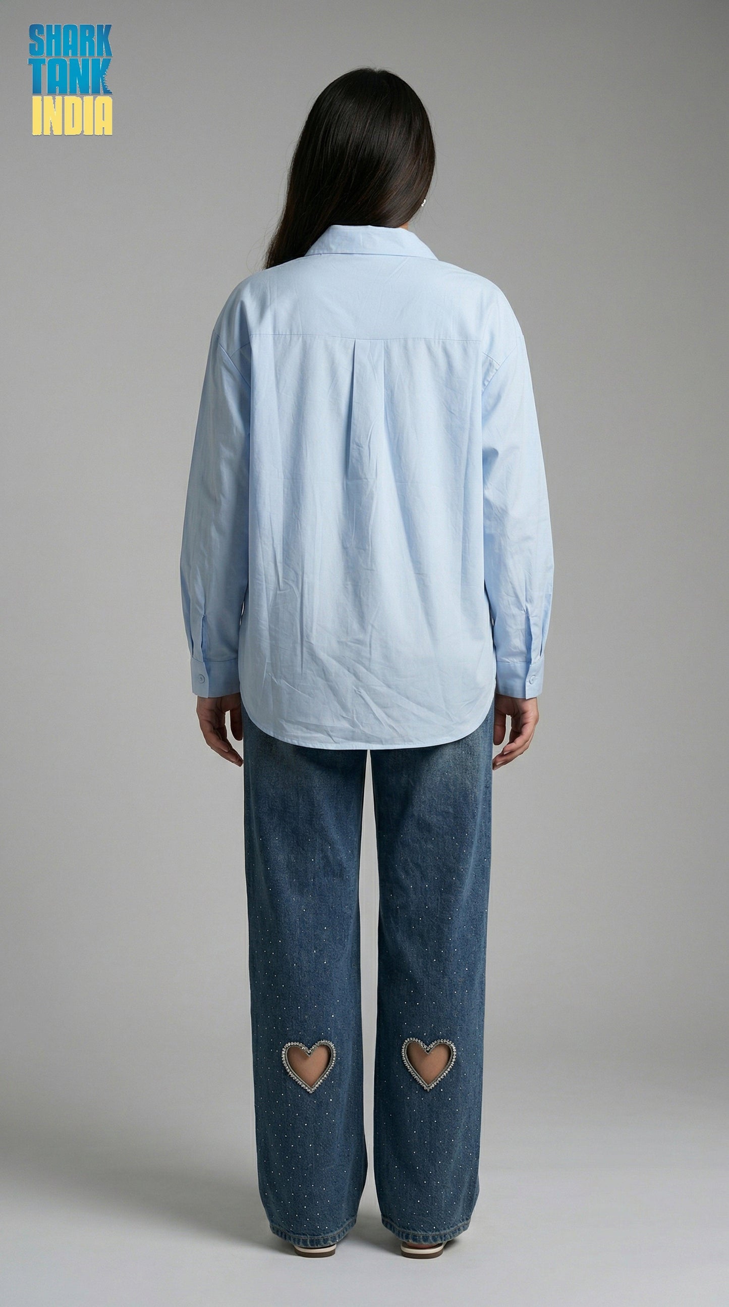 Person wearing a light blue shirt and blue jeans with heart cutouts on a gray background