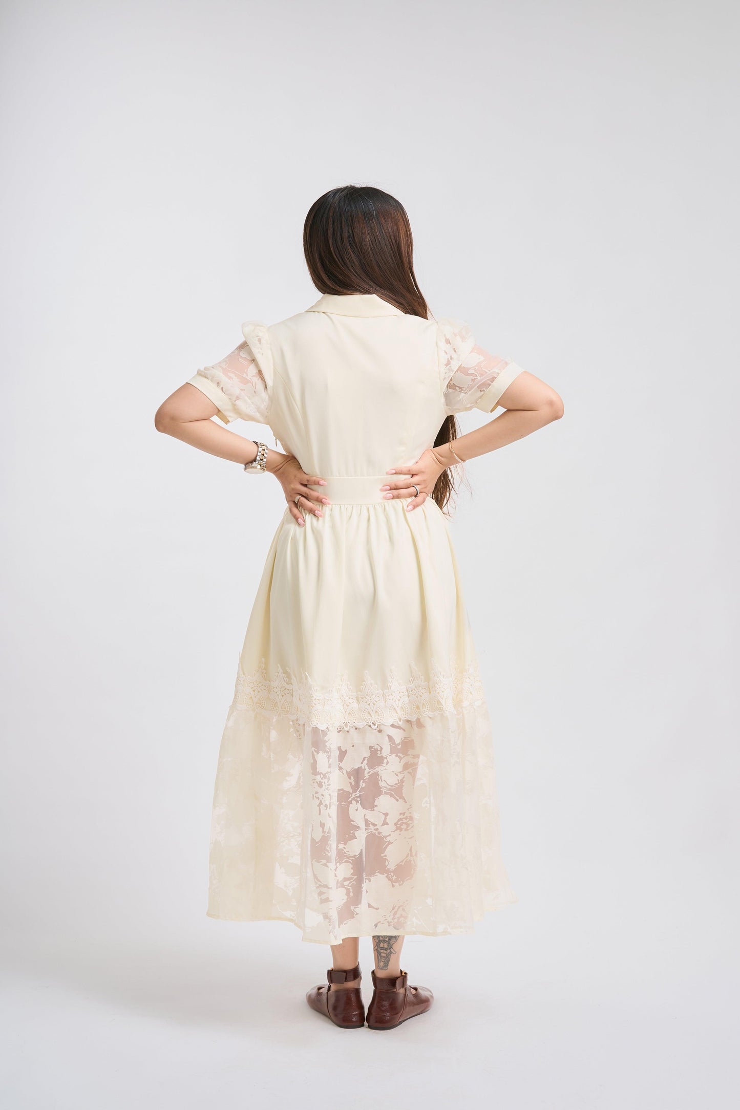 Woman wearing a long, light-colored dress with lace details on a white background
