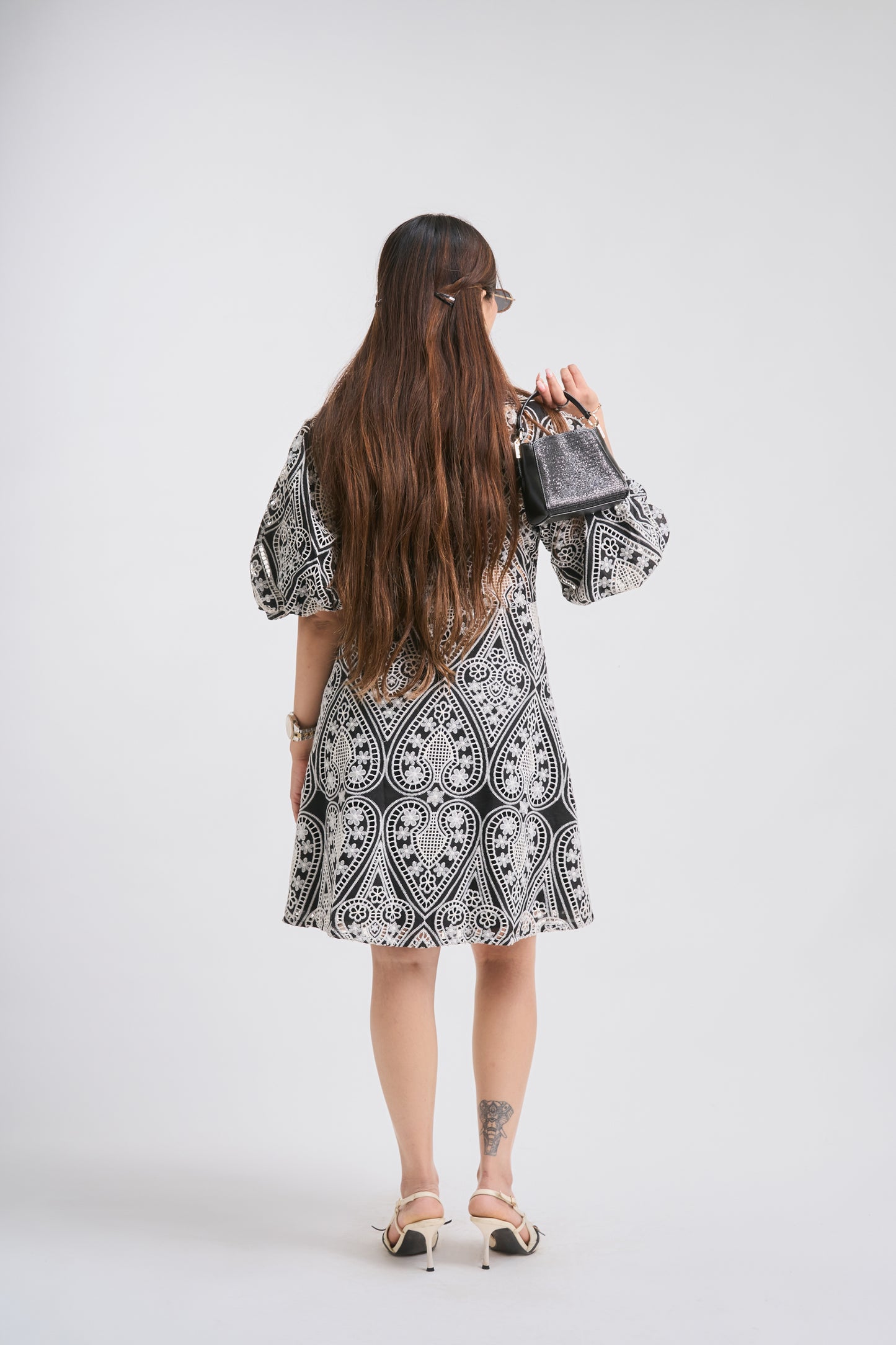 Woman wearing a black and white patterned dress holding a handbag on a white background