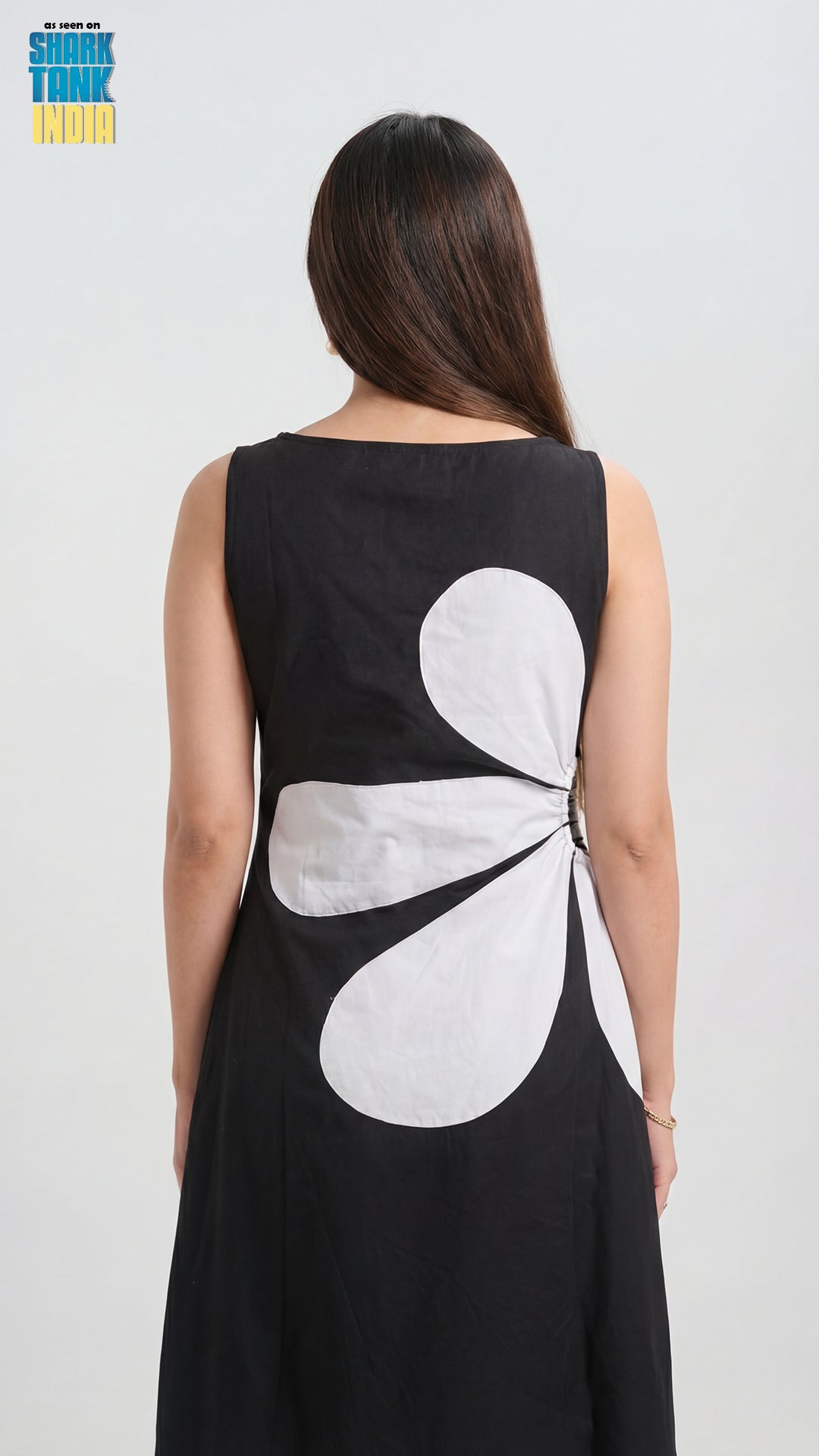 Woman wearing a black dress with a white floral design on the back against a white background