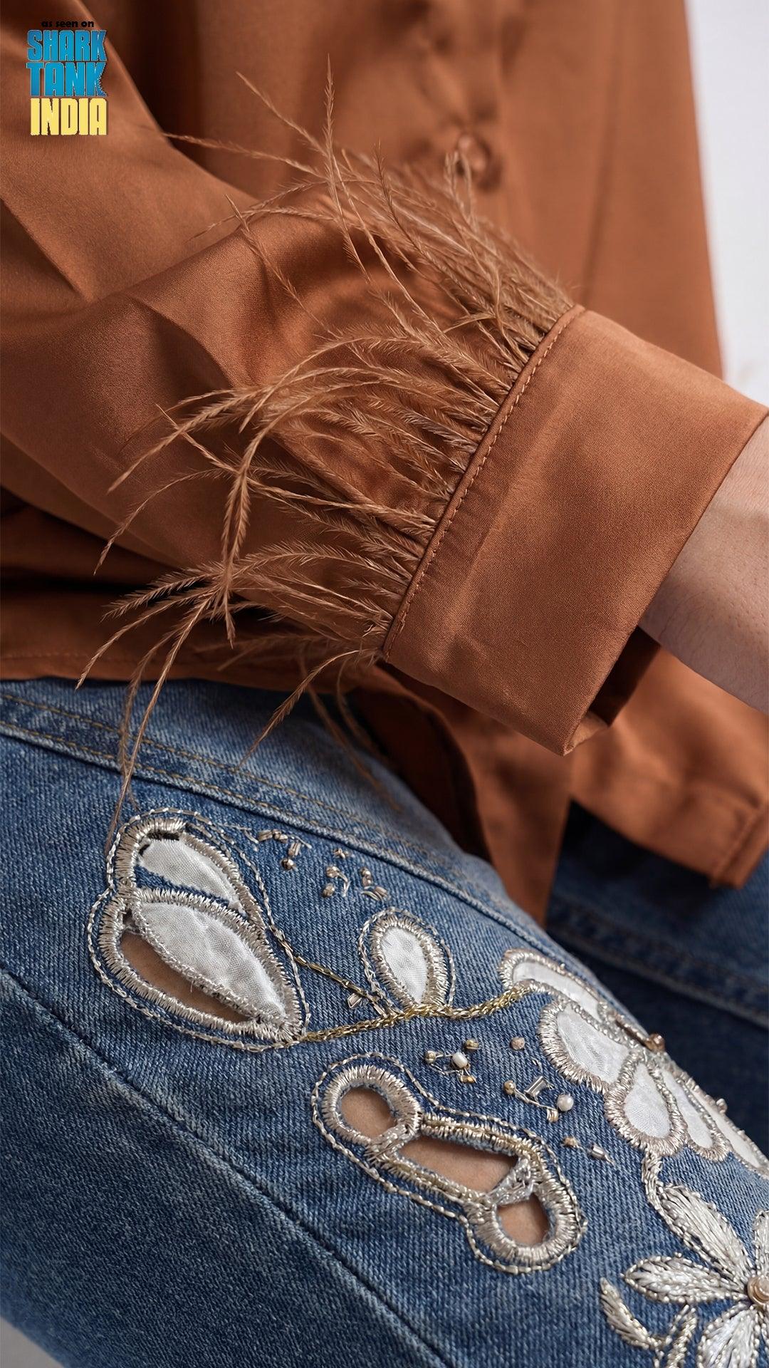 Close-up of a brown jacket with fringes and blue jeans with floral embroidery.