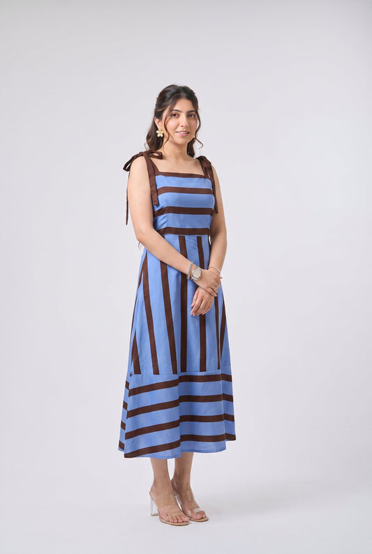 A woman modeling a sleeveless midi dress with vertical blue and dark brown stripes, standing against a light gray studio background.
