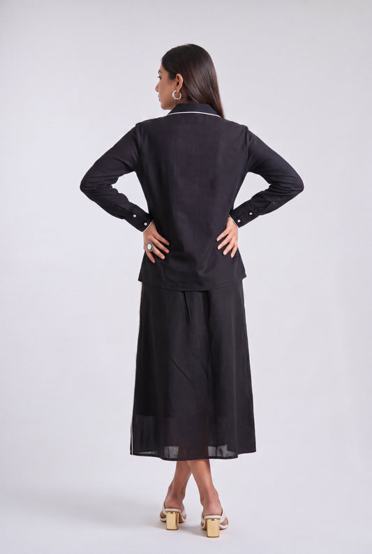 A woman is shown from the back wearing a black long-sleeve top and matching wide-leg skirt set, photographed against a plain light gray studio background.