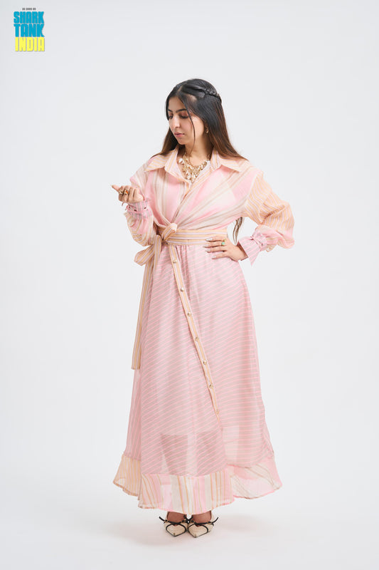 A woman modeling a light pink and white striped long-sleeve maxi dress with a beige belt, standing against a plain white studio background. A 'Think Tank India' logo is visible in the top left corner.