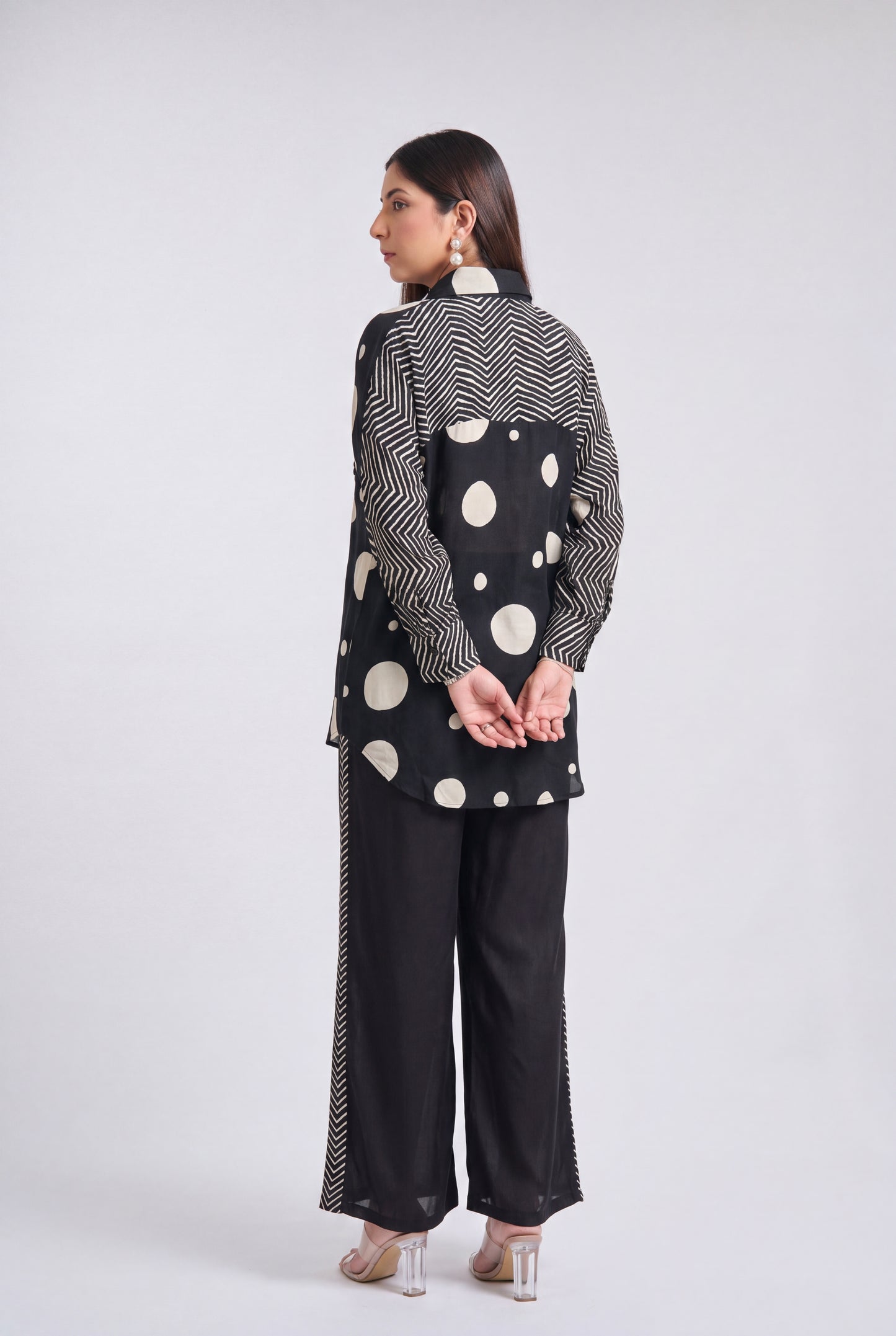 A woman is shown from the back wearing a black and white patterned kurta and wide-leg trousers set, standing against a light gray studio background.