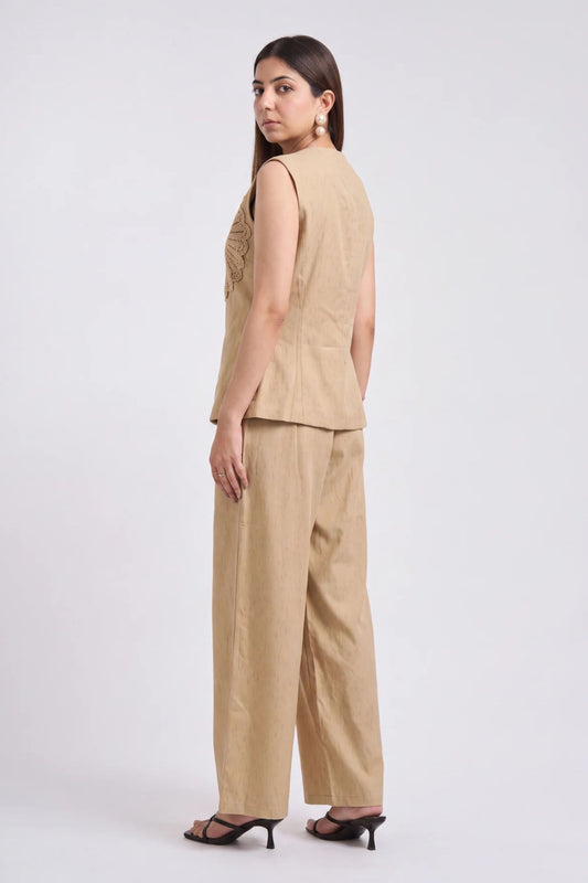 A woman modeling a beige sleeveless vest and matching wide-leg trousers, shown from the back against a plain light gray studio background.