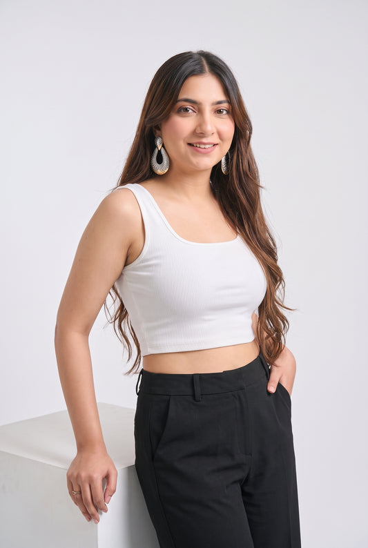 A woman posing in a white scoop-neck crop top and black trousers against a light gray studio background.