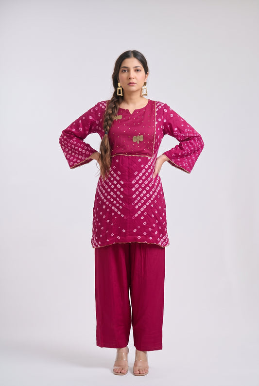 A woman modeling a magenta pink kurta set with white printed patterns and gold embroidery, paired with matching wide-leg pants, against a light gray studio background.