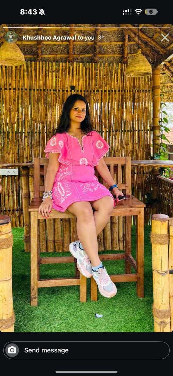 Woman in a pink dress sitting on a wooden chair in front of a bamboo wall.